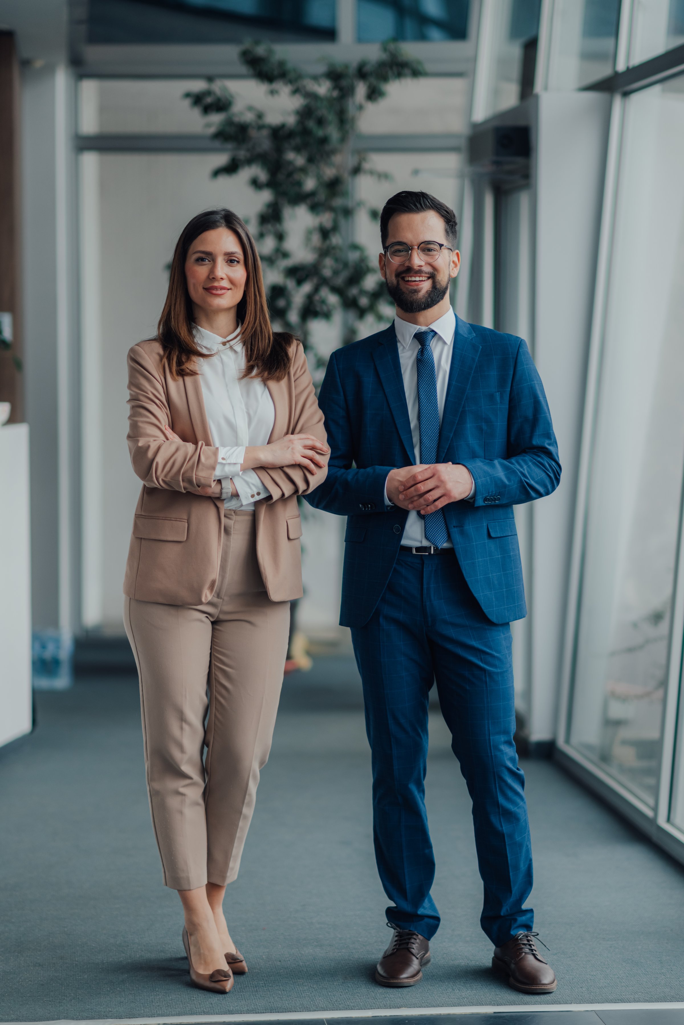 Full-length portrait of two business people smiling and posing confidently in a modern office environment