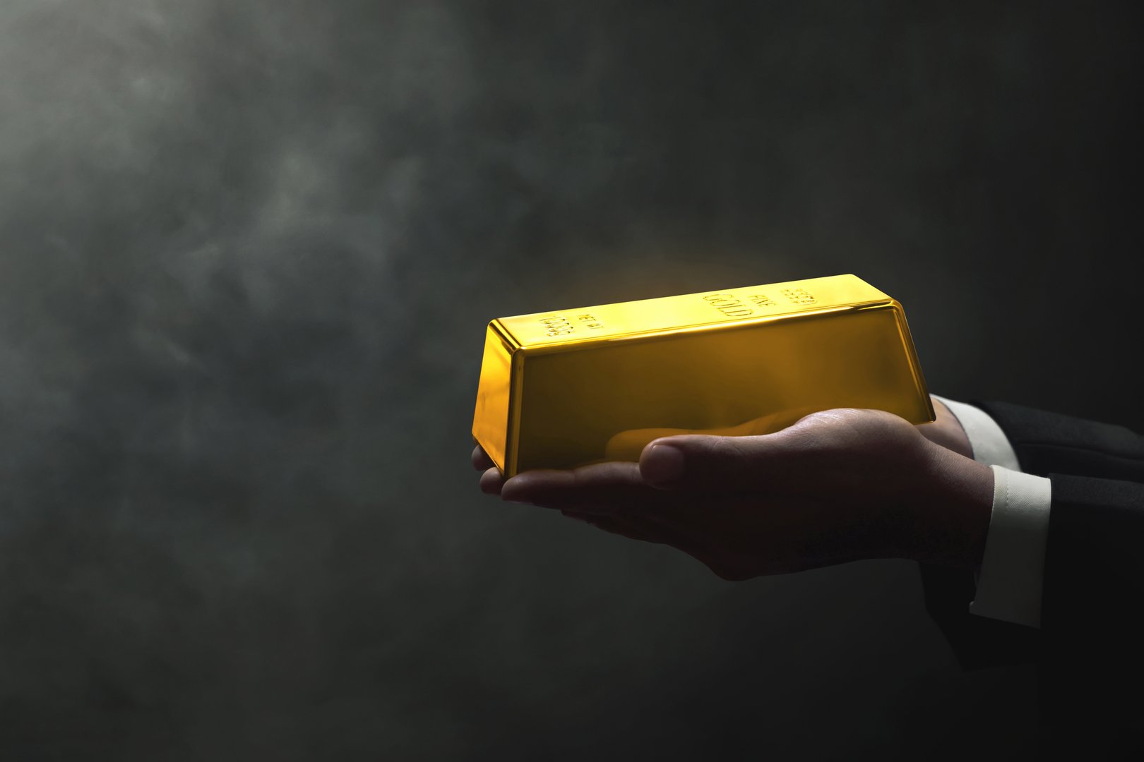 Businessman hands holding shiny gold bar on dark background