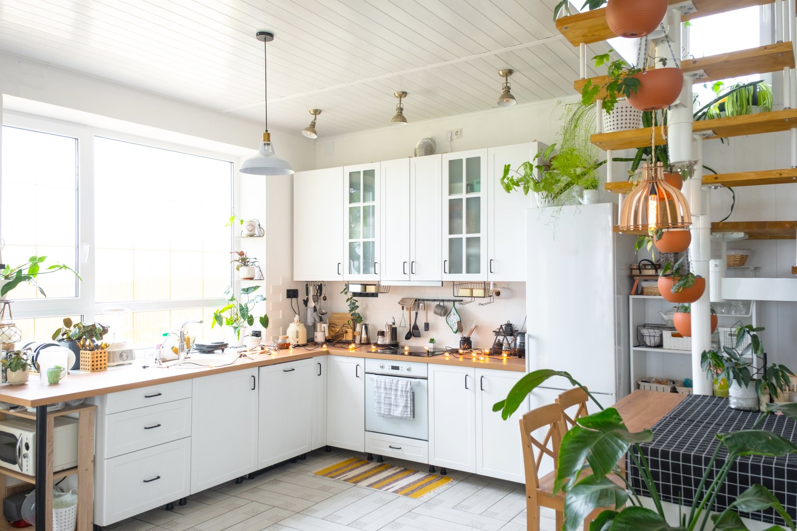 The general plan of a light white modern rustic kitchen with a modular metal staircase decorated with potted plants. Interior of a house with homeplants