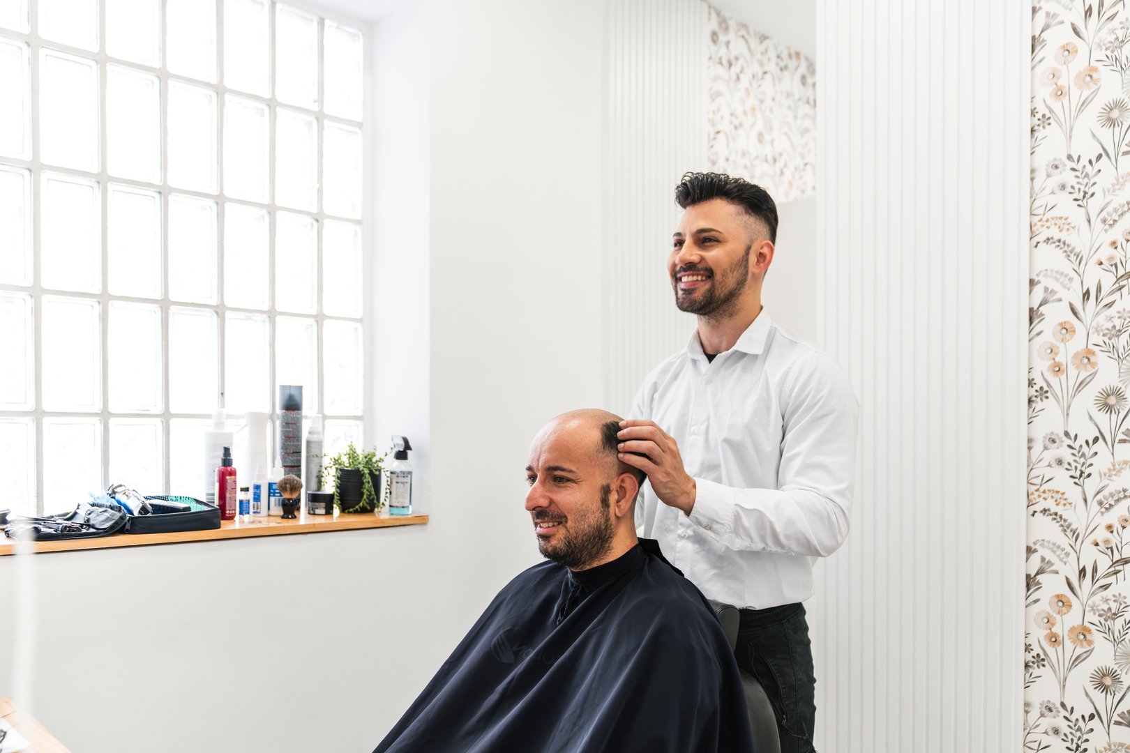 Hairdresser applying a hair replacement system to a balding customer in a hair salon, offering a solution for hair loss and boosting confidence