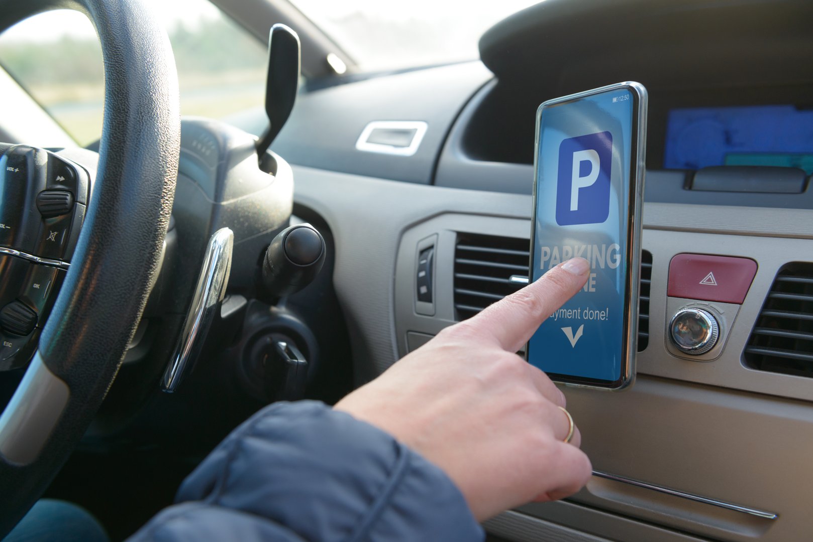 Driver using smartphone app to pay for parking in the paid parking zone in a city