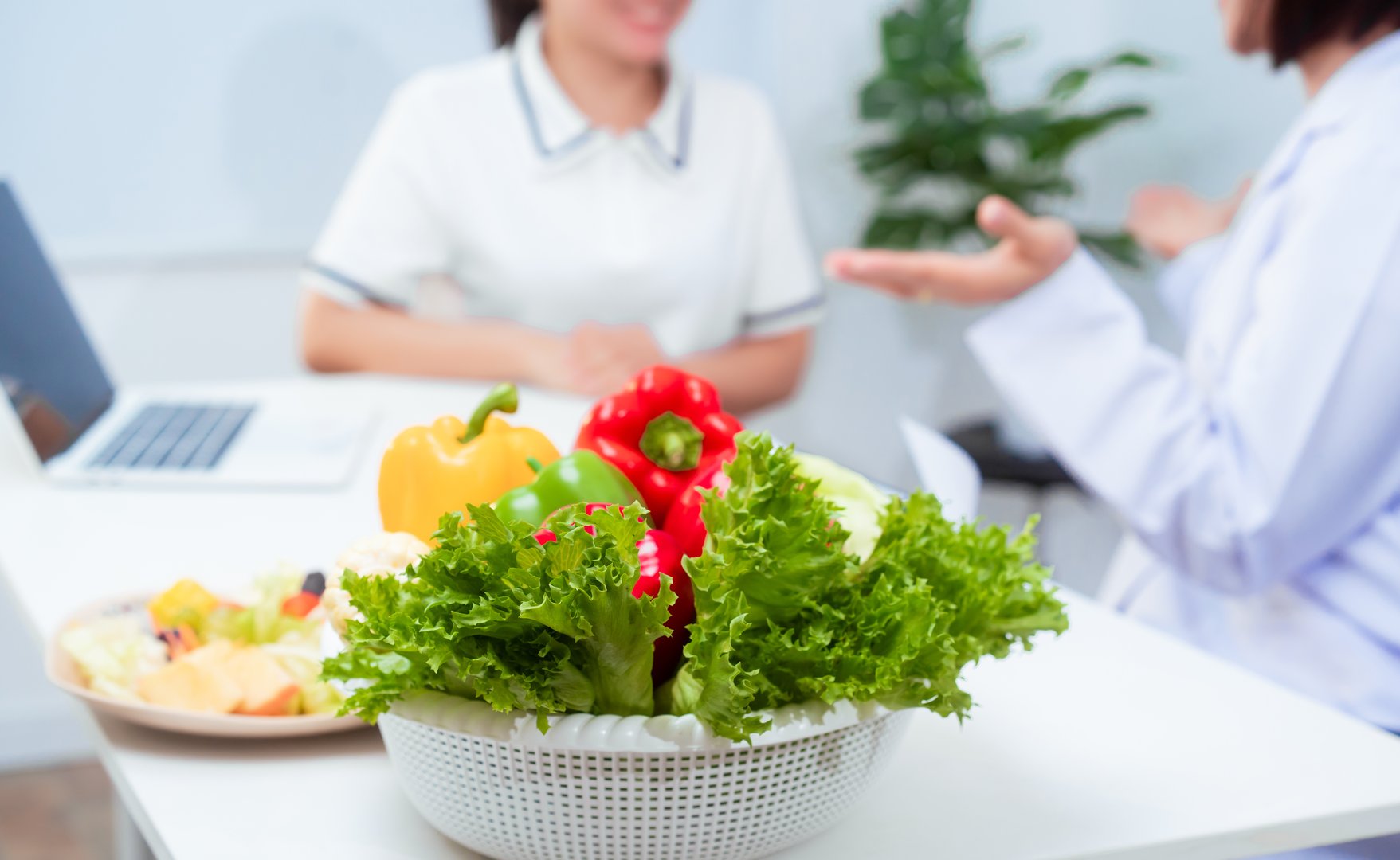 Professional Asian female nutritionist giving nutritional counseling to female patient sitting at clinic table discussing diet, health goals, meal plans and strategies for long-term wellness