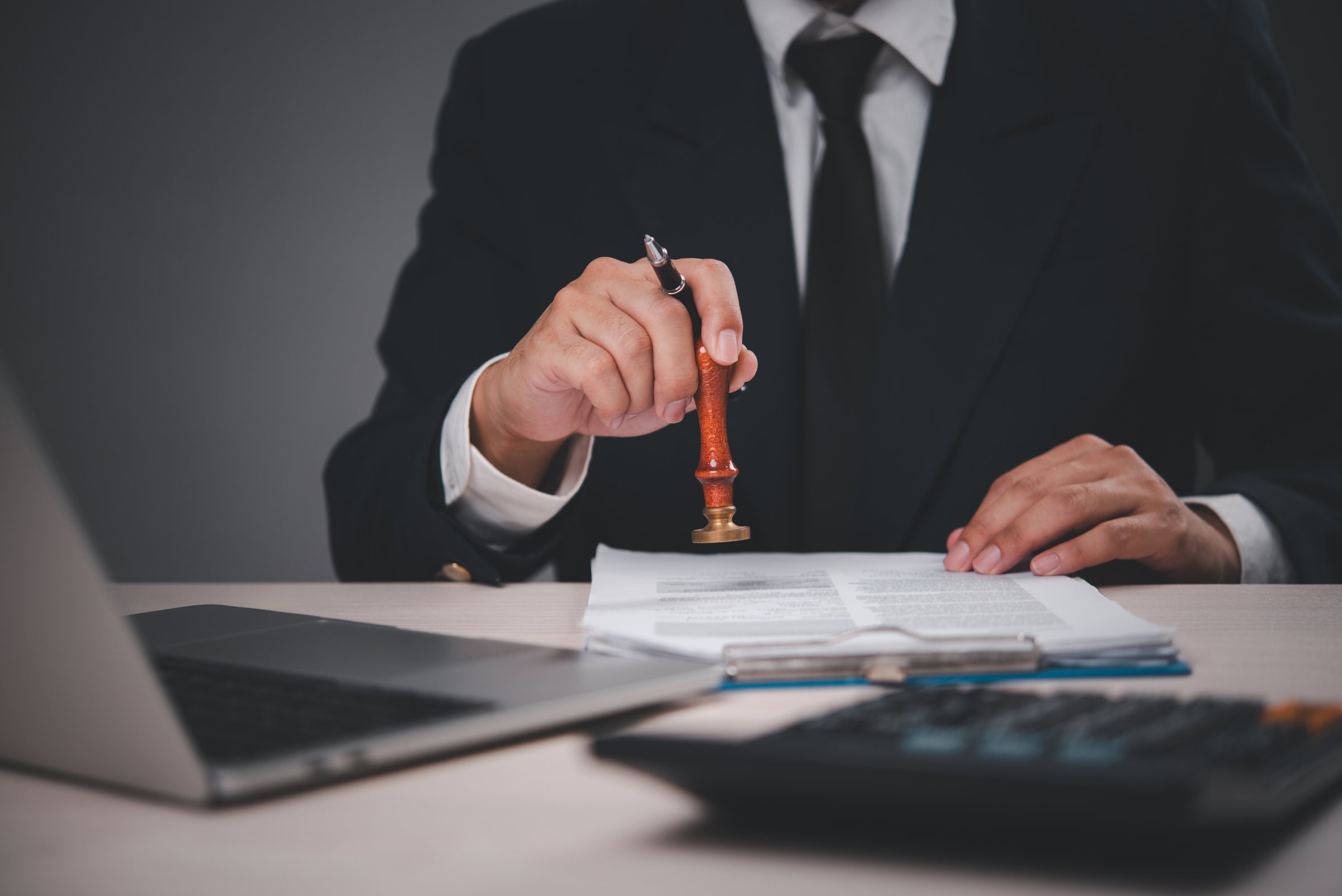 businessman in a suit stamping documents at a desk. Hand holding stamp, giving approval. Professional, authoritative action. Suitable for business, finance, legal,