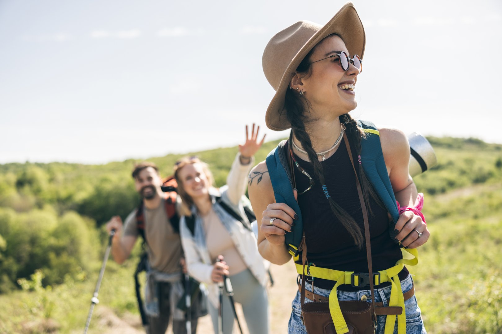 Three cheerful friends enjoying sunny day while walking and hiking in countryside.