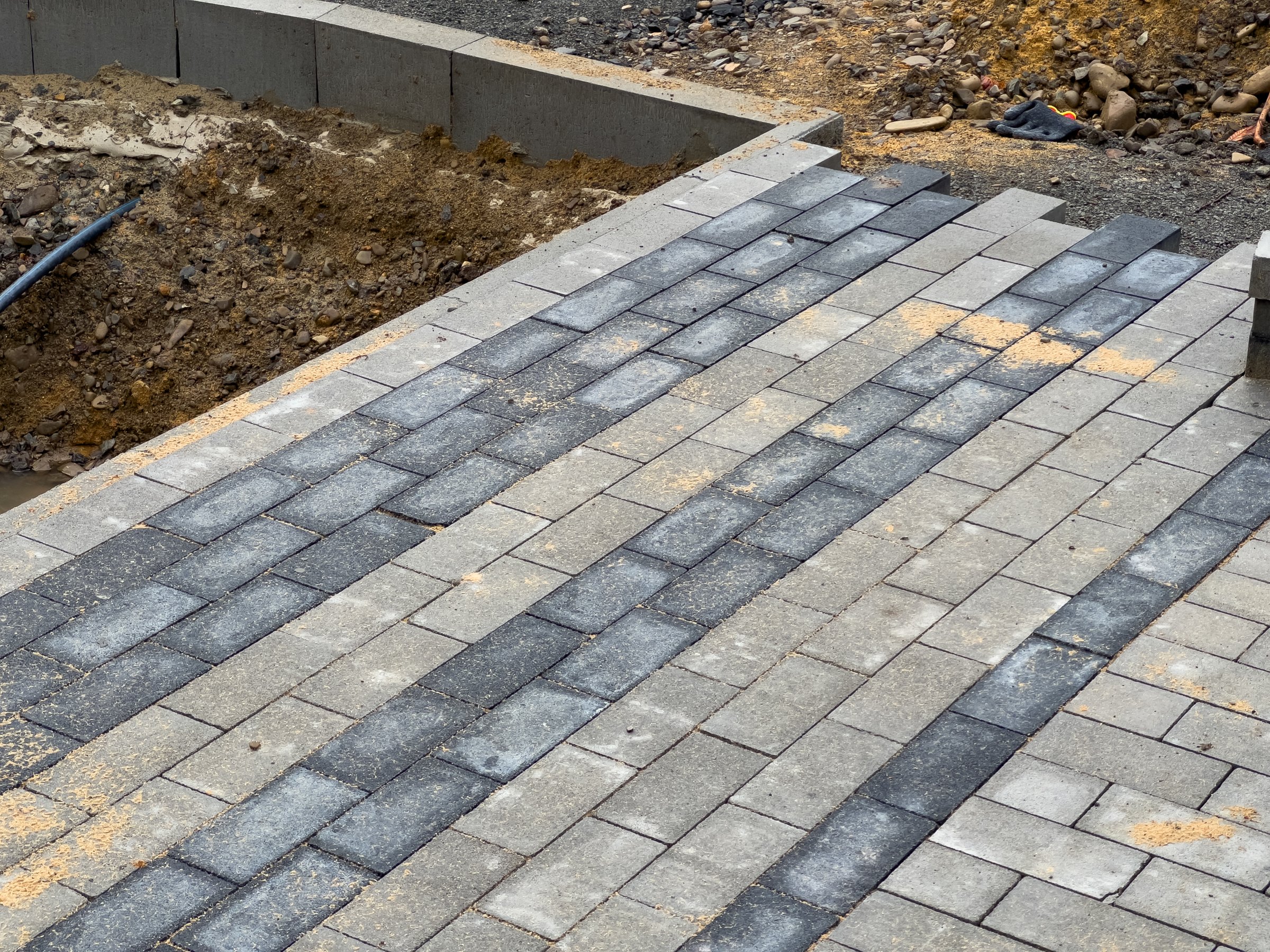 A team is actively laying paving stones to create a durable pathway in a residential area. The work is taking place during the day, showcasing the construction process.