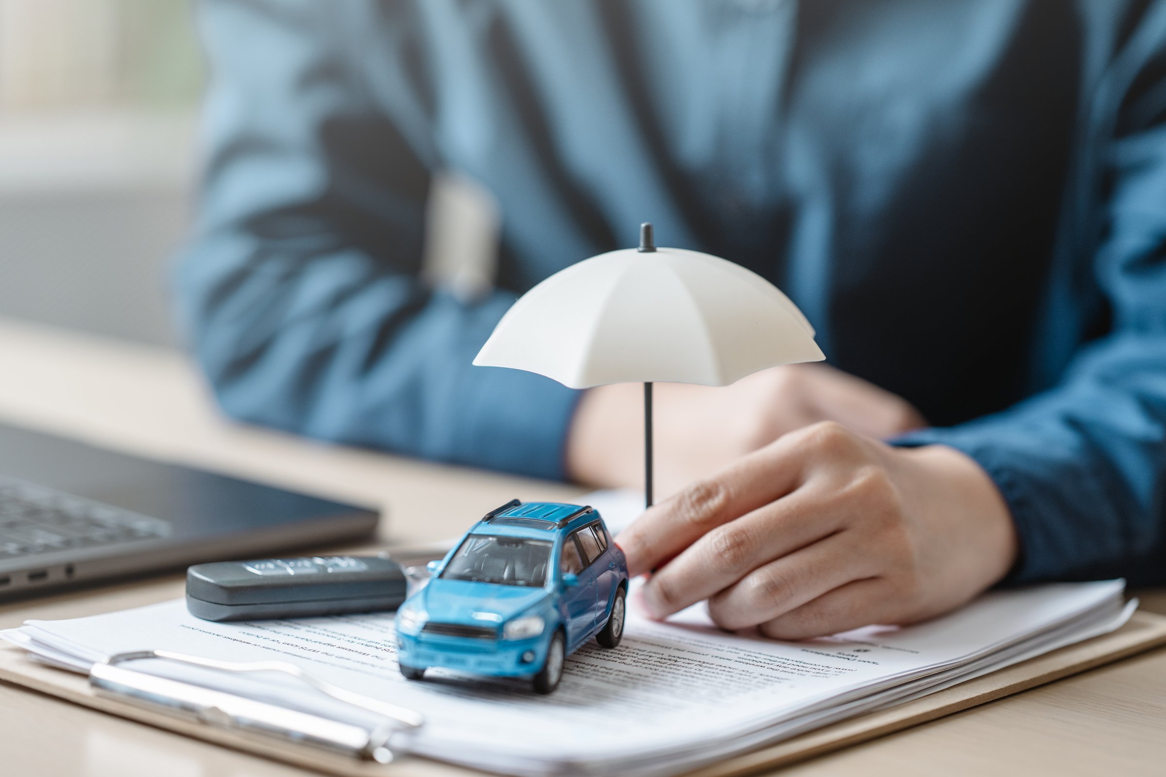 Car insurance protect concept. Insurance agent. Insurance protection concept. A person is holding a blue car under an umbrella. The umbrella is white and is placed on top of a piece of paper.