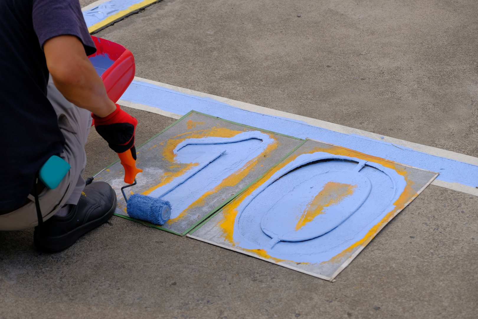 Specialist painter painting the number of parking lots blue lines striping in a car park. Profestional painter man at work with a roller, Blank for text with copy space.