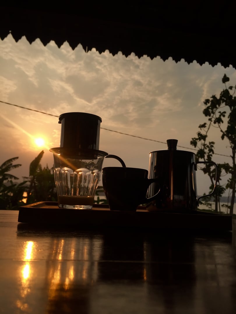 a small teapot, cup and vietnamese drip maker sat on the table, blocking the sunlight