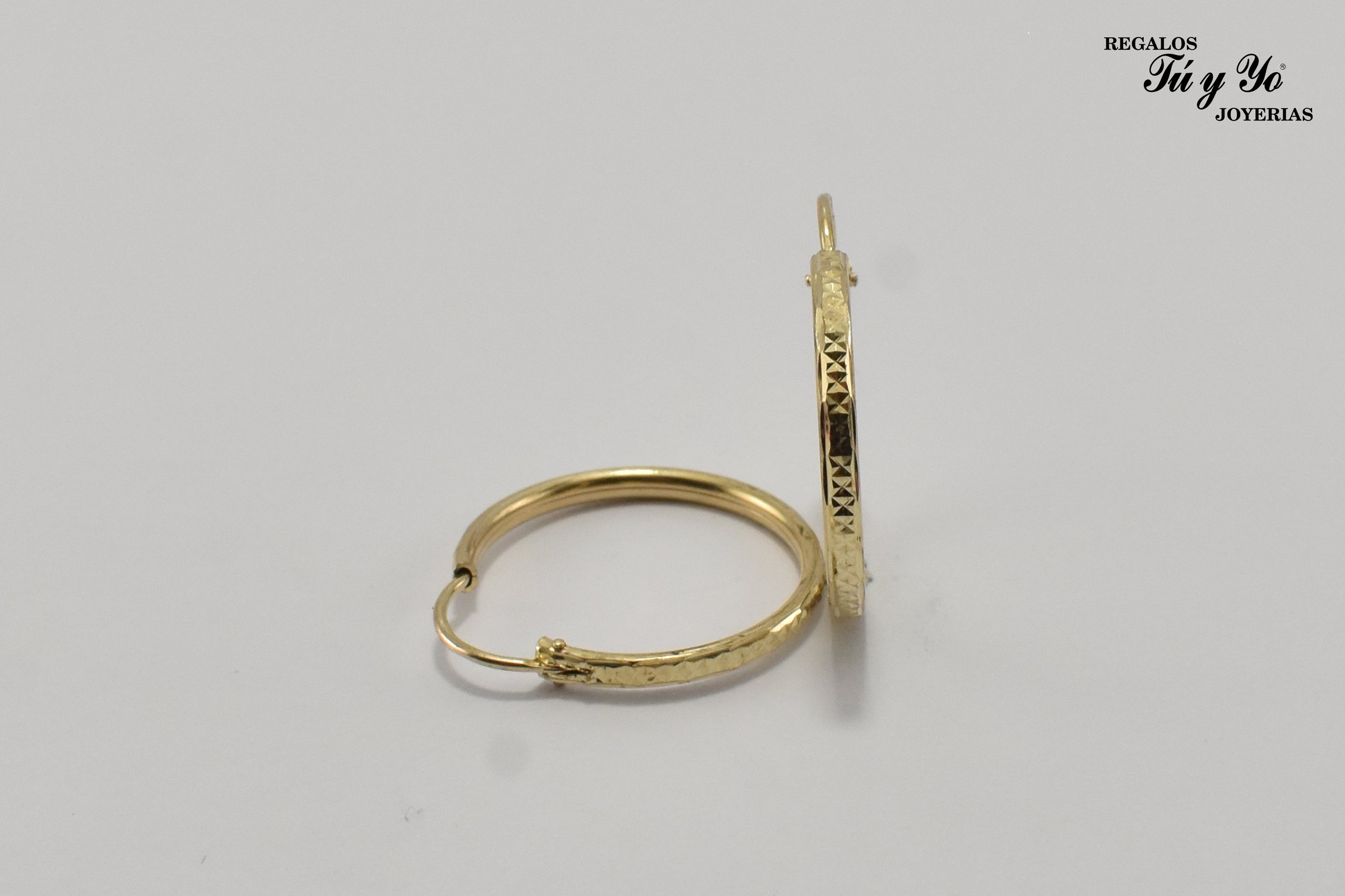 Two gold hoop earrings with engraved patterns, positioned upright and lying flat, on a white background.