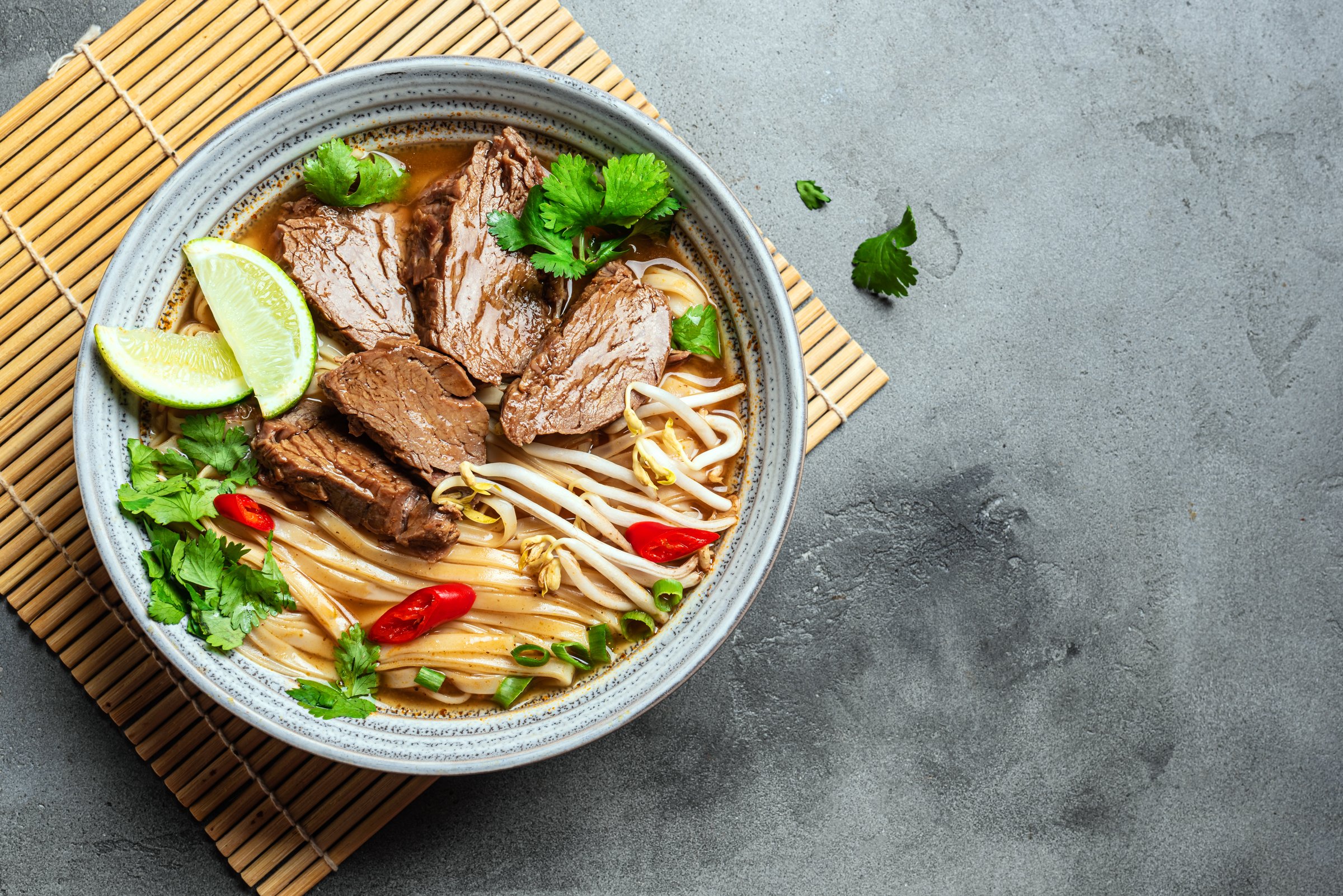 Pho Bo Vietnamese soup, bowl of fresh asian soup with rice noodle, beef, herbs, soy sprouts and chili on concrete background, top view, copy space. Asian food.