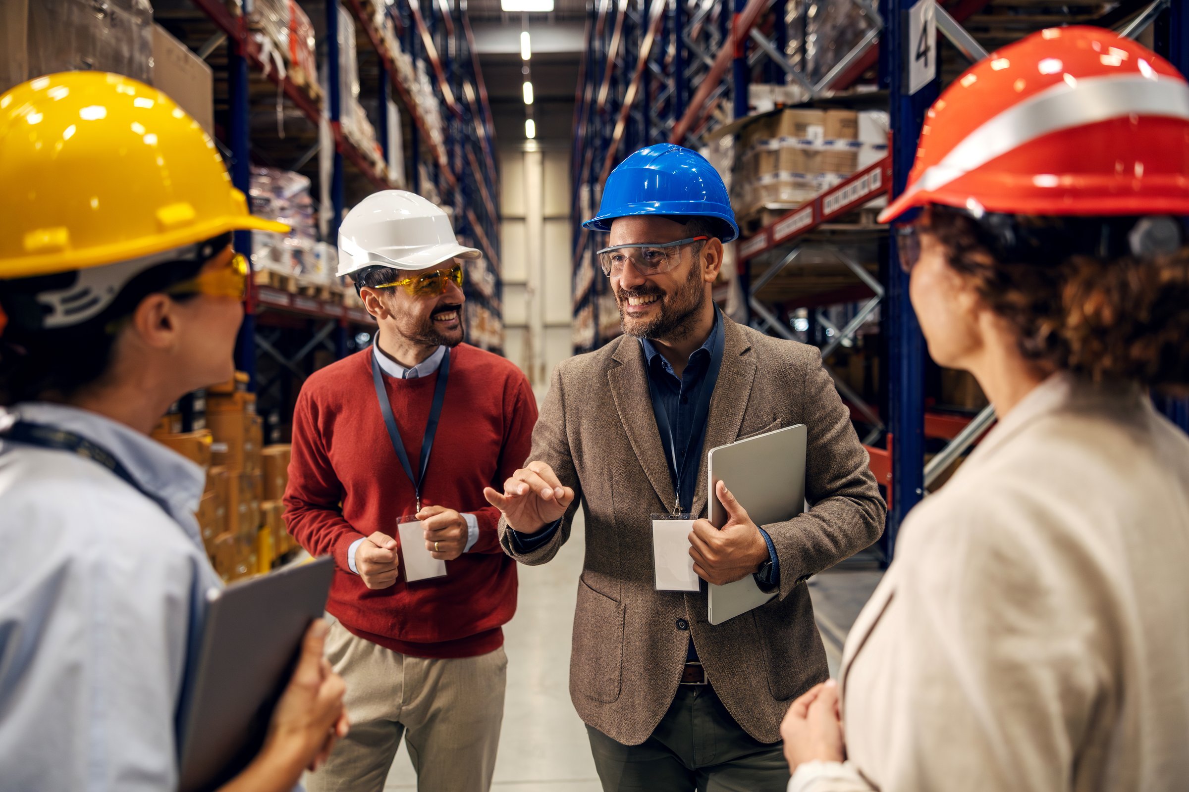 Warehouse team, including managers and workers, discussing operations and safety while walking through a large storage facility