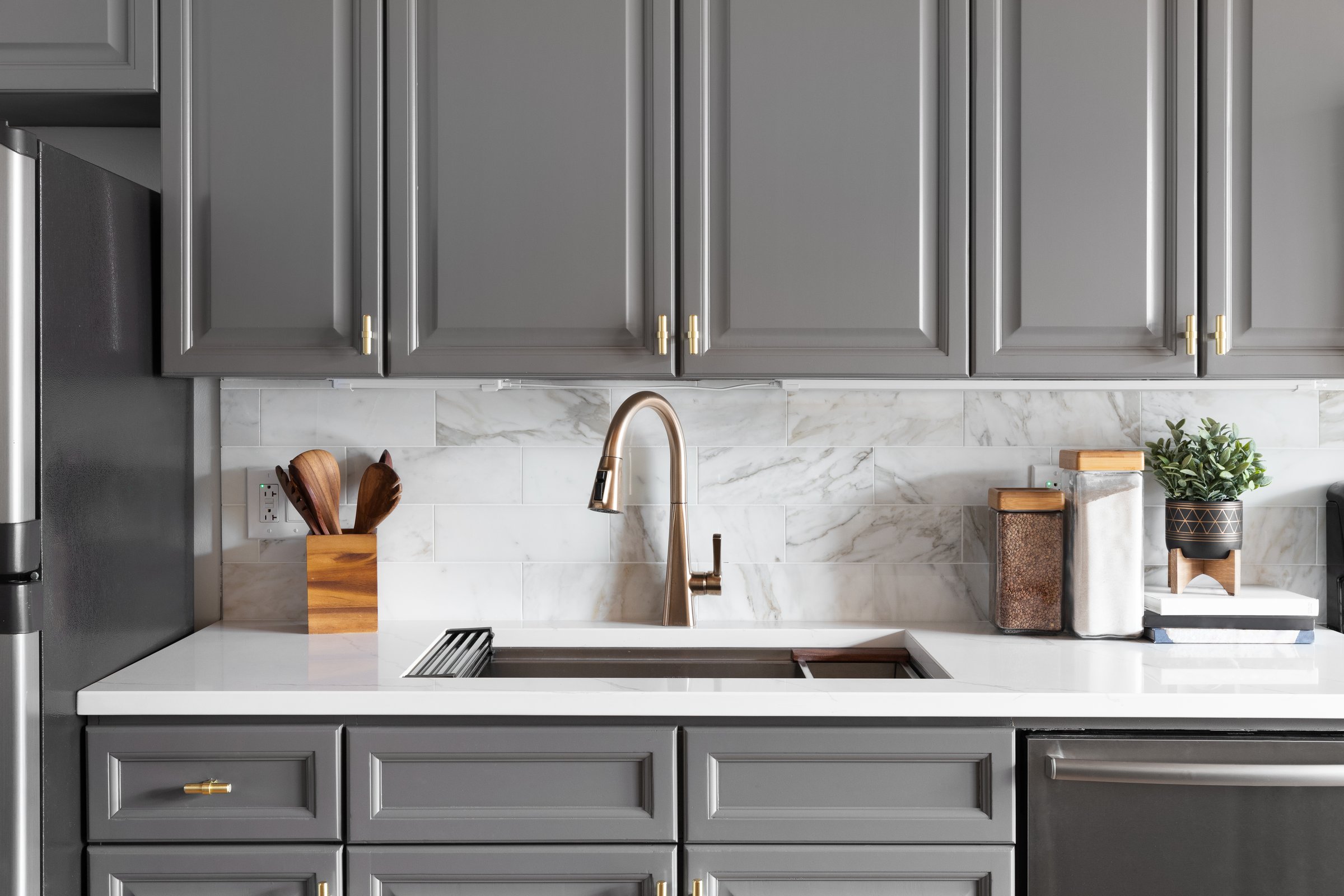 Kitchen sink detail with grey cabinets and marble countertop