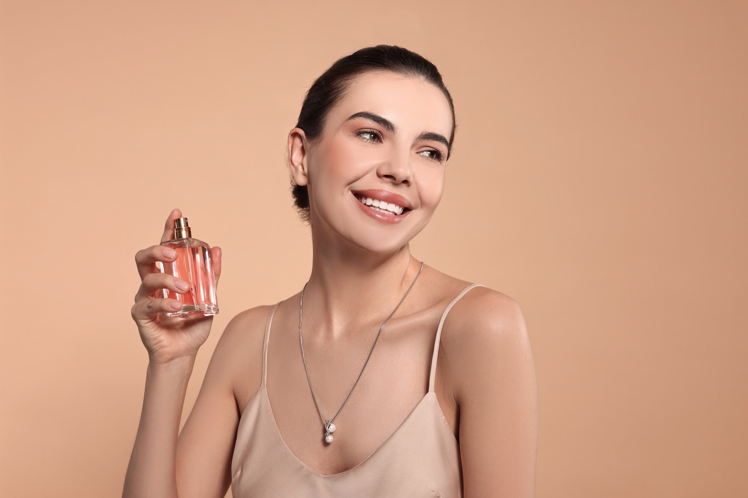 Smiling woman with bottle of perfume on beige background