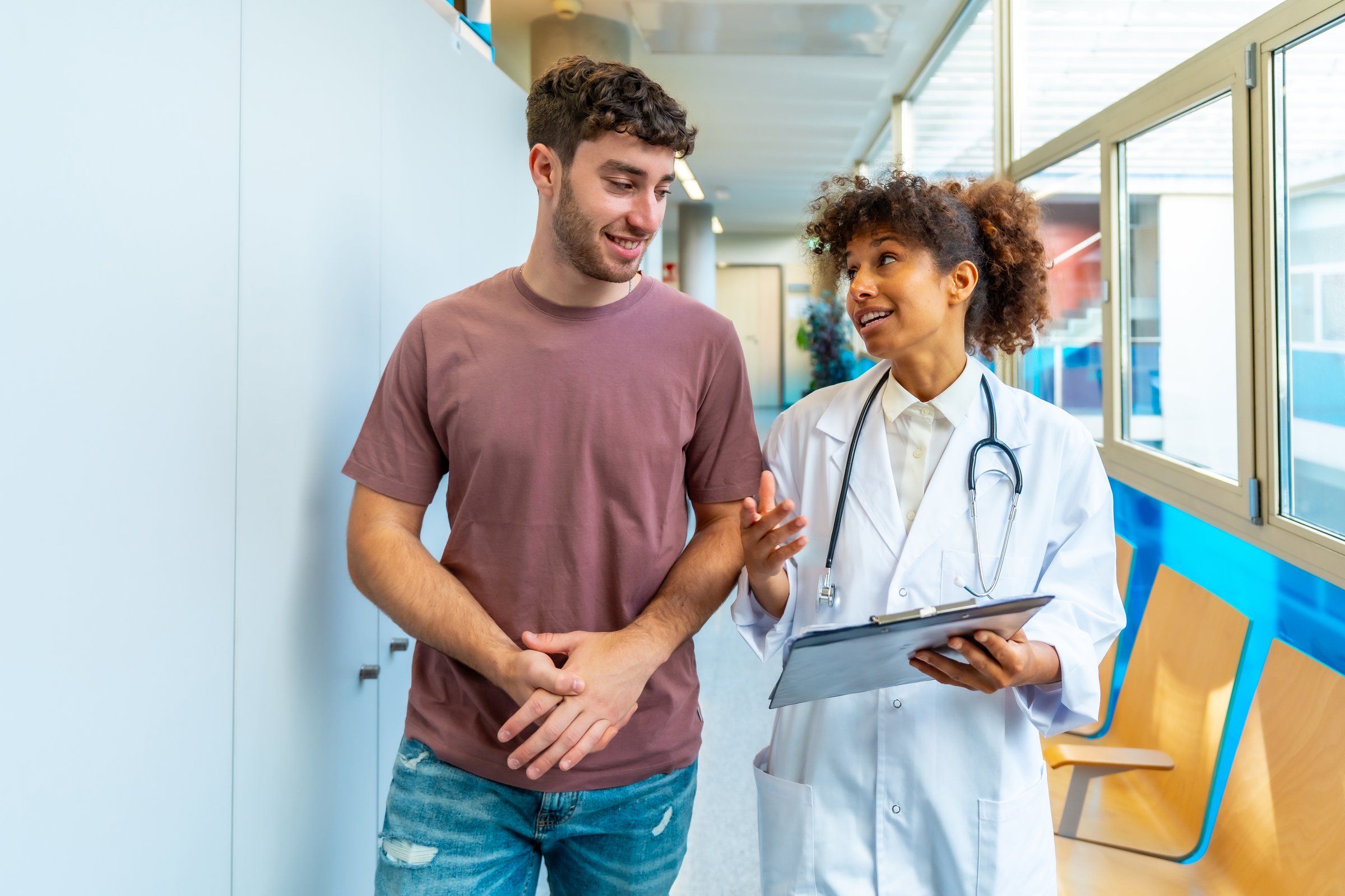 Female doctor walks and talks with a young male patient, explaining his diagnosis, in a modern hospital corridor