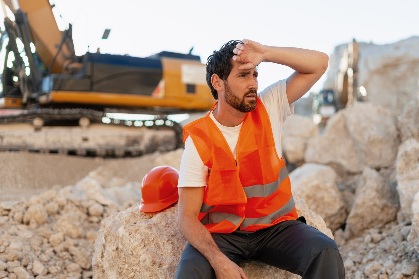 Exhausted construction worker resting in a quarry, wiping sweat from his forehead while taking a much-needed break from the heat