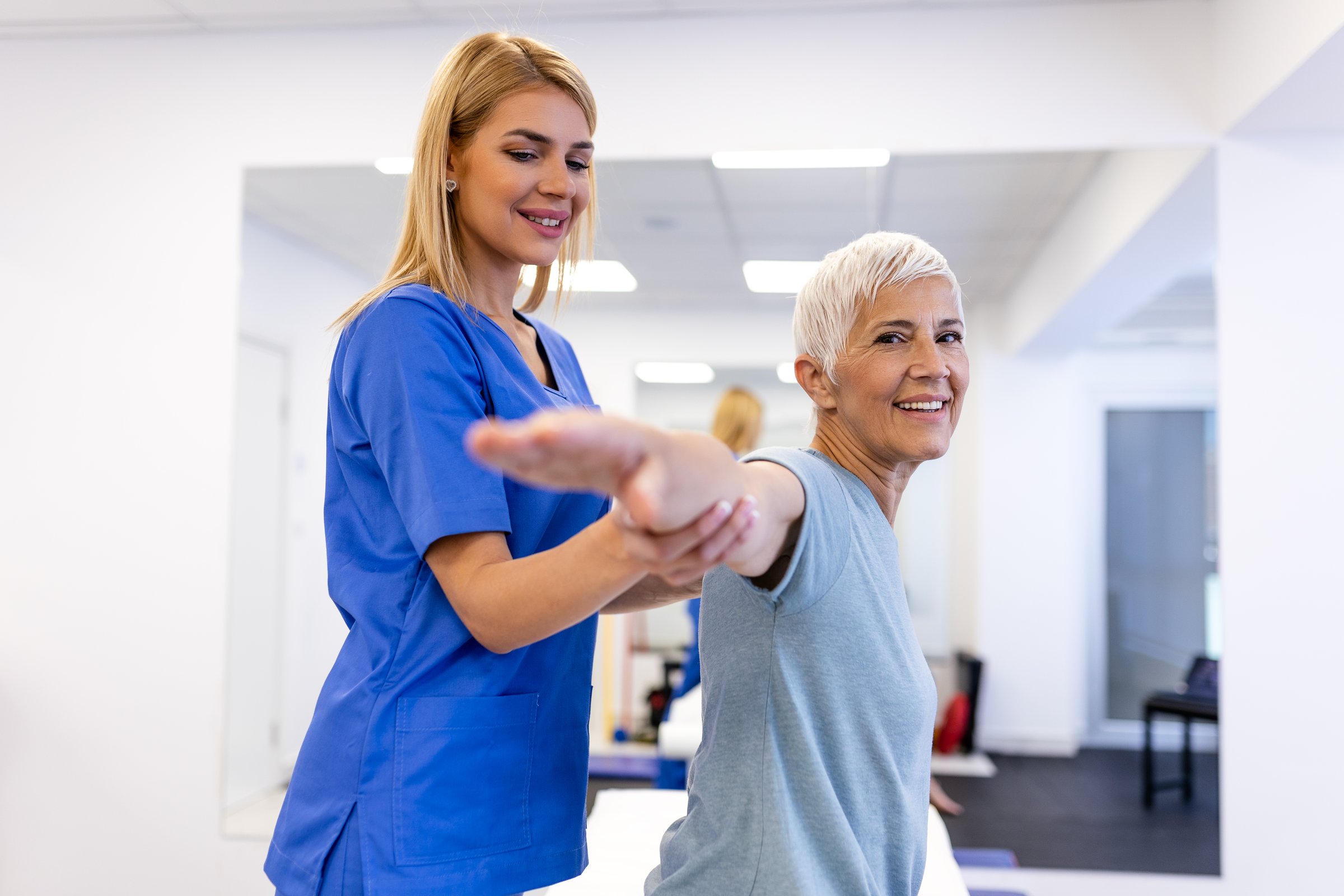 Doctor orthopedic teaching senior woman to do osteoporosis treatment exercise in modern clinic. Physiotherapist helping female patient during muscle rehabilitation physiotherapy