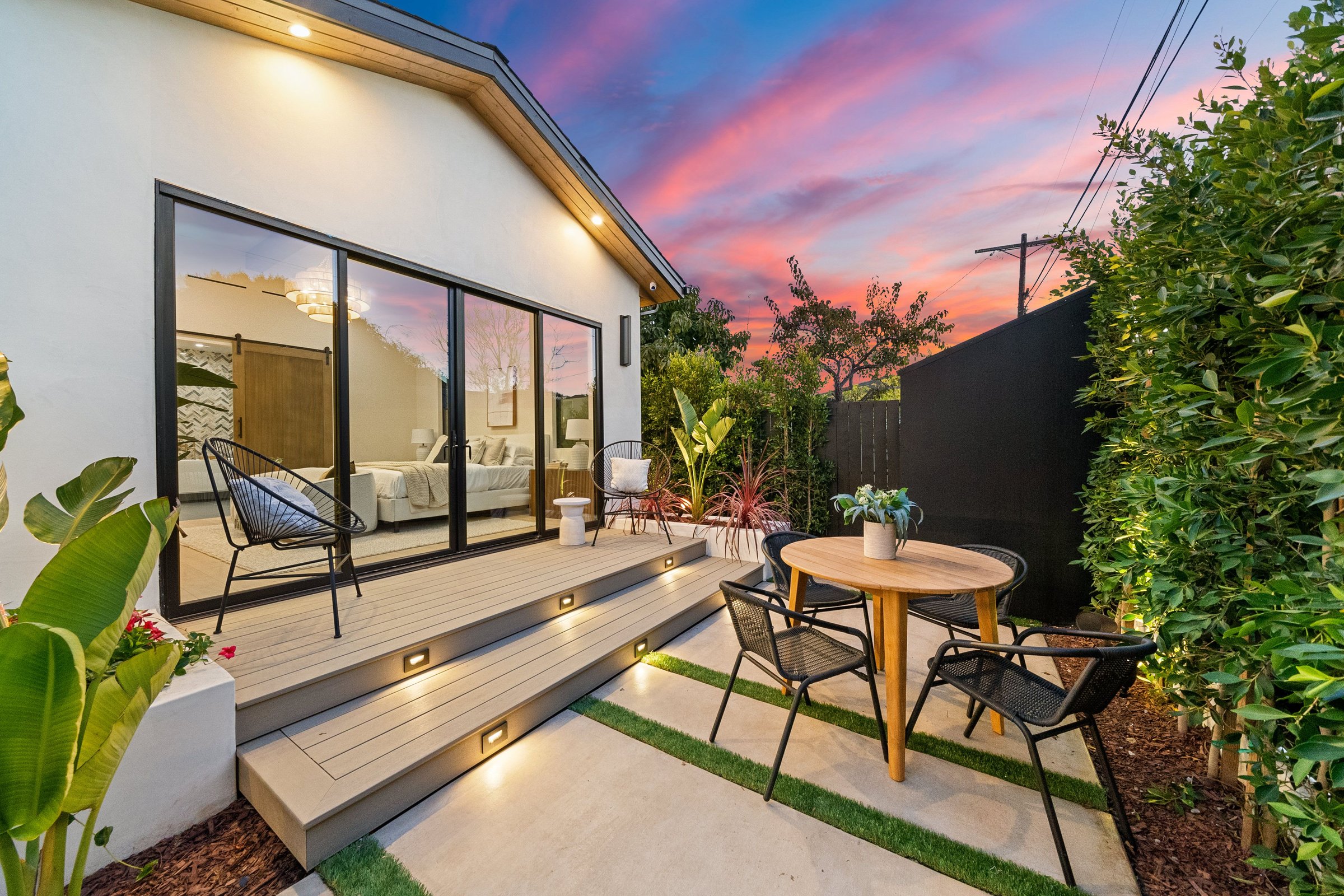Modern patio with stylish furniture and plants at sunset, featuring a cozy outdoor seating area and glass doors leading indoors.