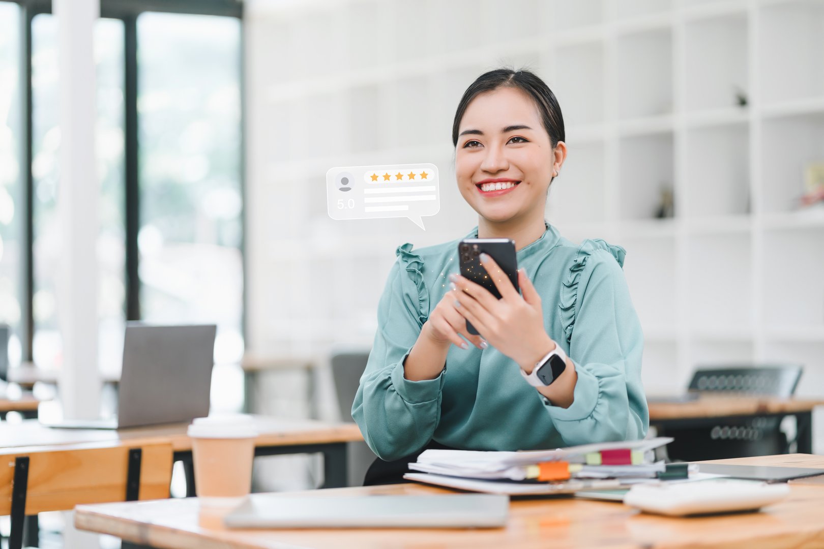 Woman in an office smiles while reading a 5-star online review on her smartphone