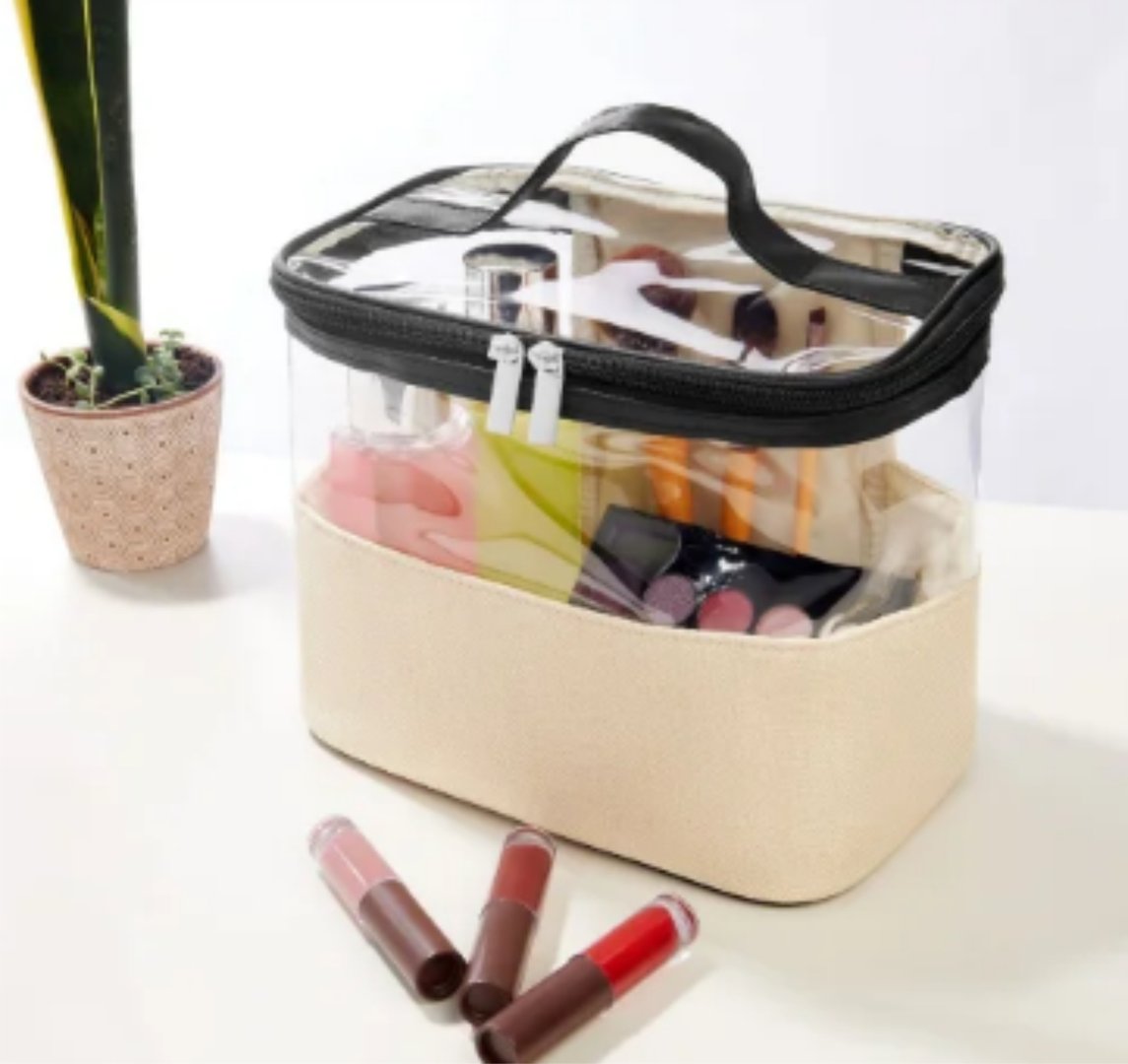 Clear cosmetic organizer with black zipper, filled with various makeup items, next to a potted plant on a white surface.