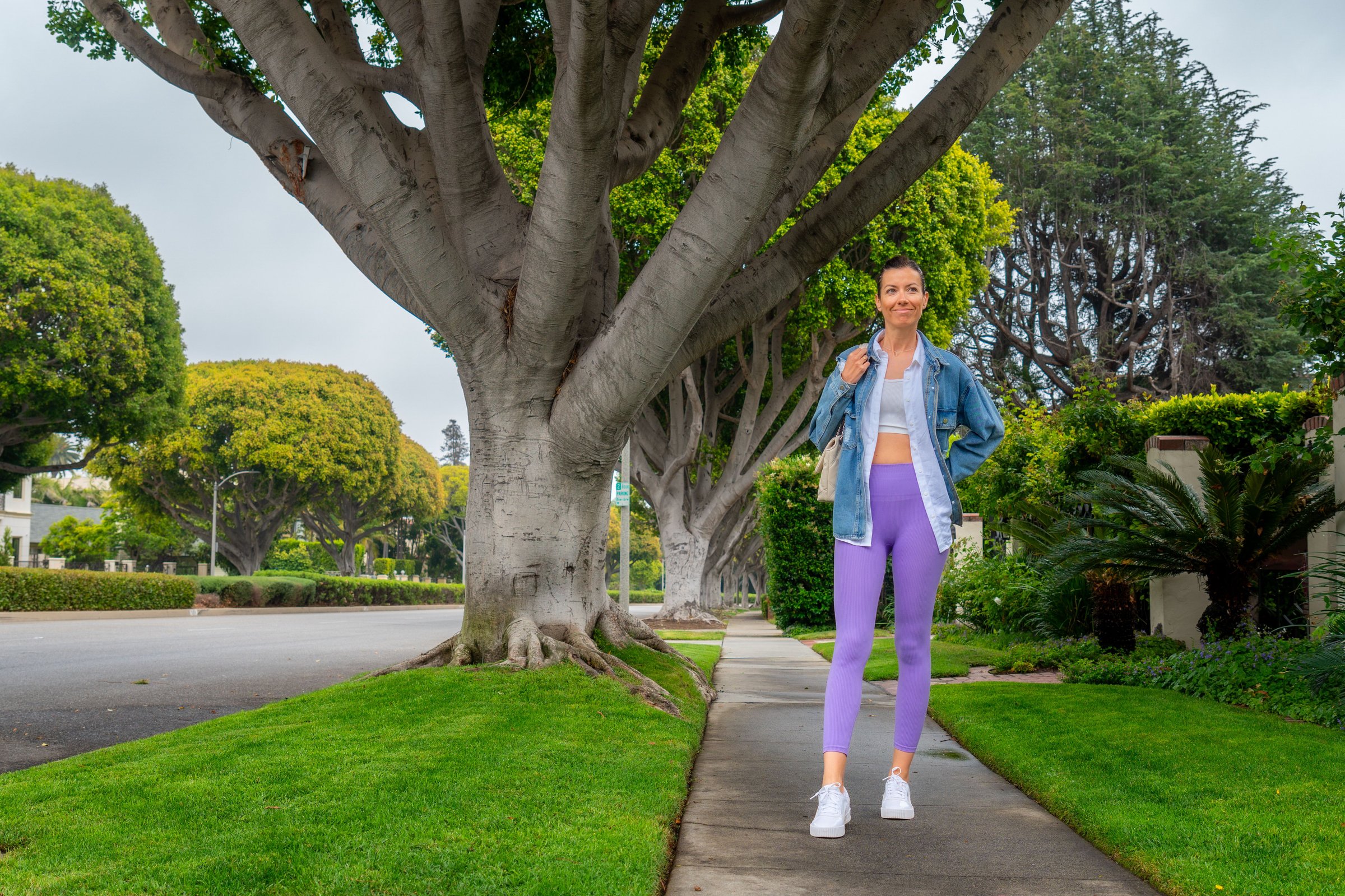 A woman in athletic wear walks along a tree-lined street, showcasing fitness and urban lifestyle.