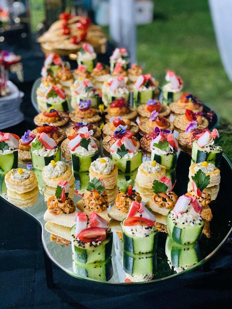An assortment of colorful, artistic appetizers arranged on a platter, featuring cucumber rolls, breads, and edible flowers.