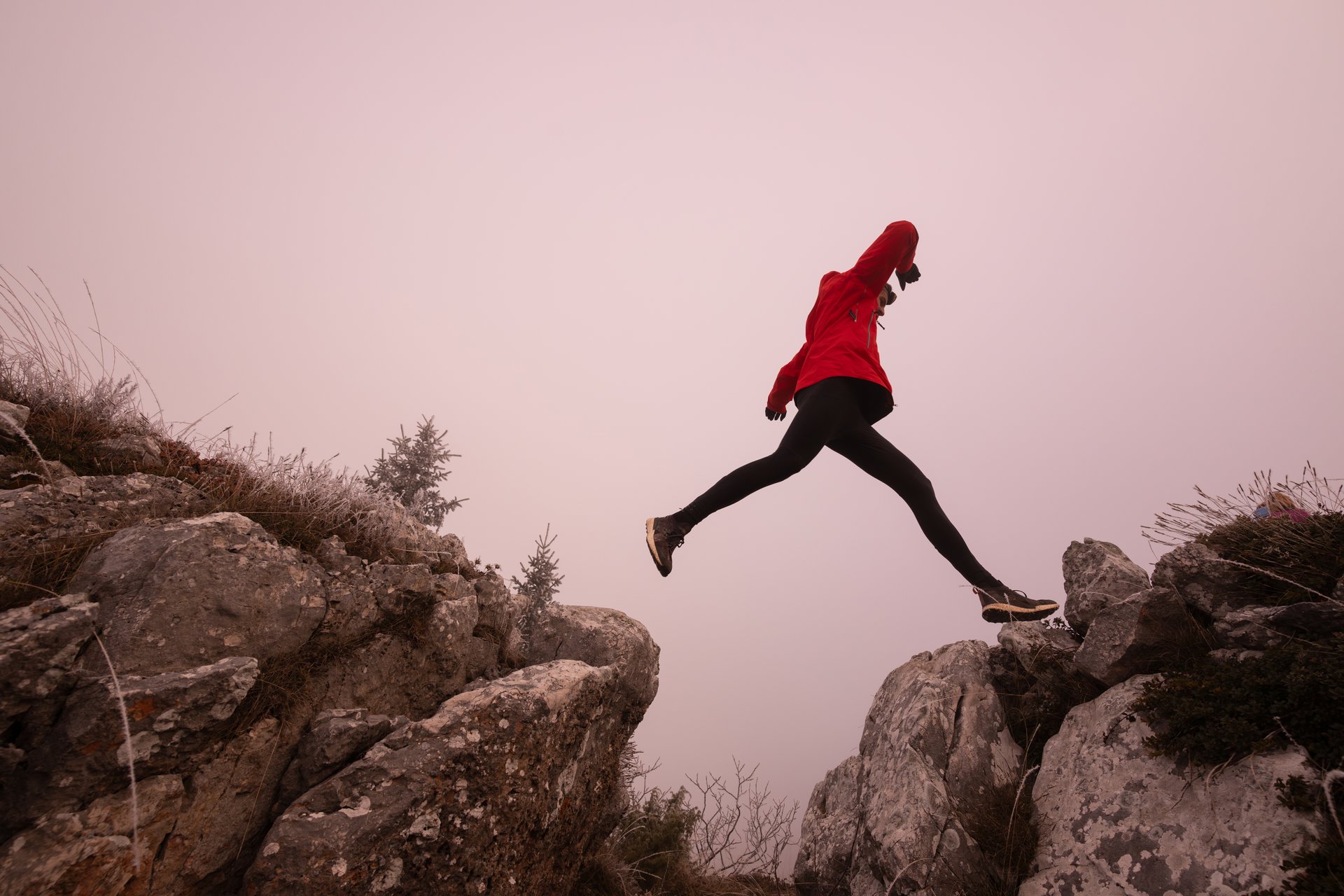 silhouette of a fitness man trail runner jumping over a cliff and running to a rocky mountain top in the early morning or night