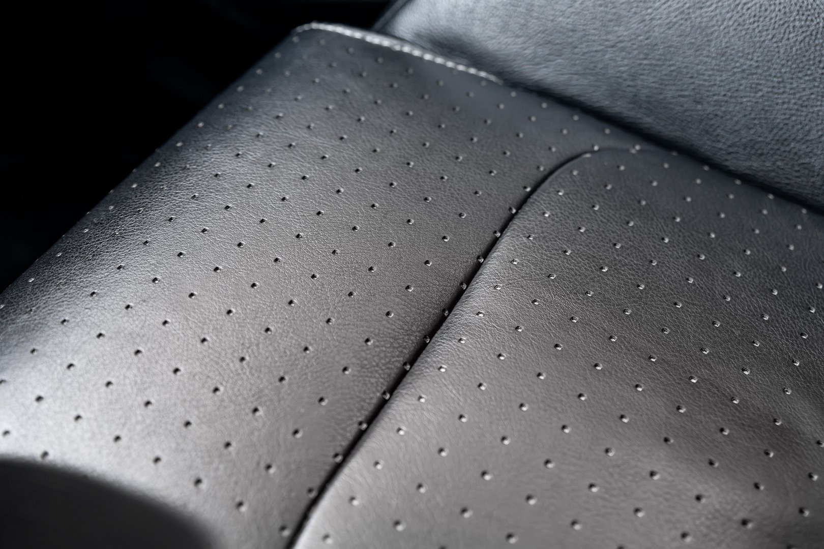 Close-up detail view of modern black perforated dotted ventilated luxury car seat. Part of dark vehicle interior. Auto detailing and leather polish skin cleaning wash and care concept.