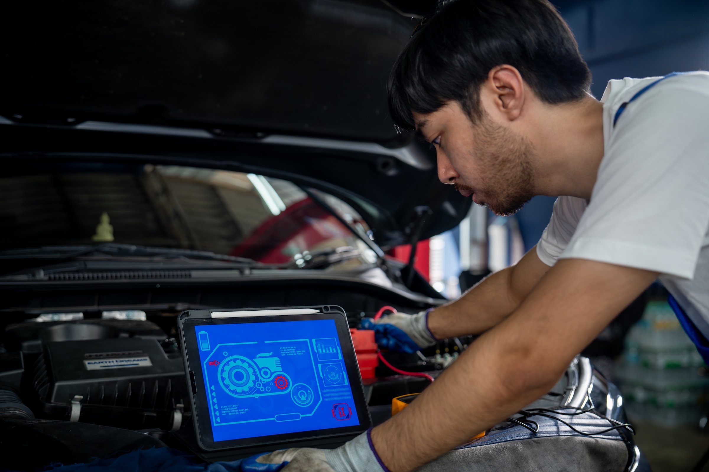 Auto mechanic using a digital tablet to inspect and maintain a vehicle in a professional garage, ensuring quality and performance.