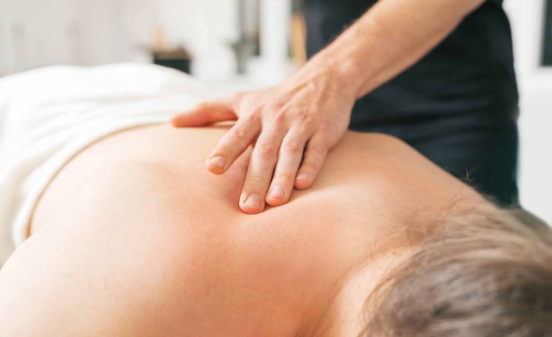Therapist's hands gently massage patient's neck and shoulders zone. Image highlights relaxation, medicine healthcare practices in clinic. Health and bodycare image concept.