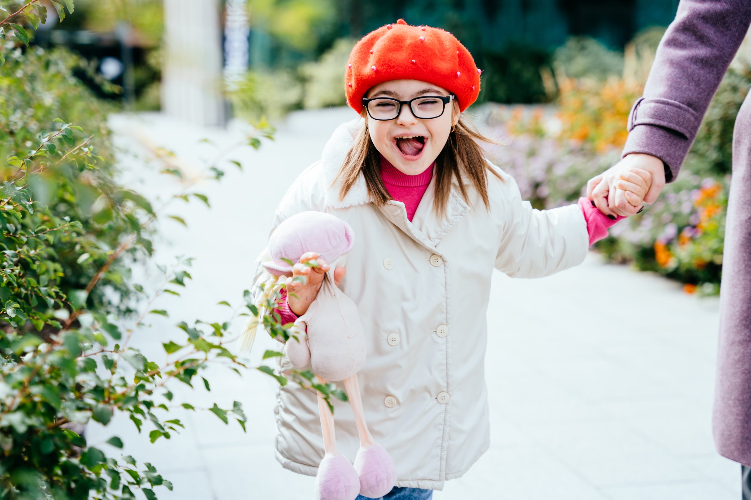Happy laughing little girl in eyeglasses with special needs holding mother's hand on a walk in autumn time outdoor. Happy family moments concept.