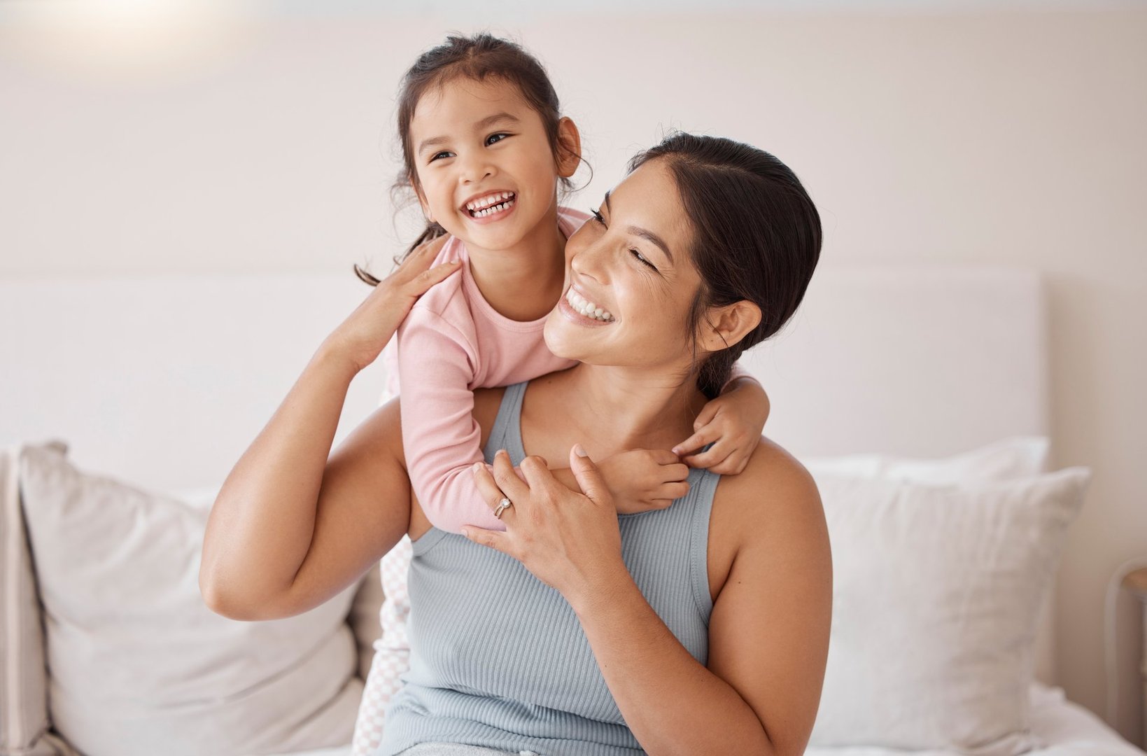 Bedroom, happy and smile of mother and girl resting and spending time together on a holiday. Relax, happiness and calm woman and her child sitting on a bed and hugging in a room of their family home.
