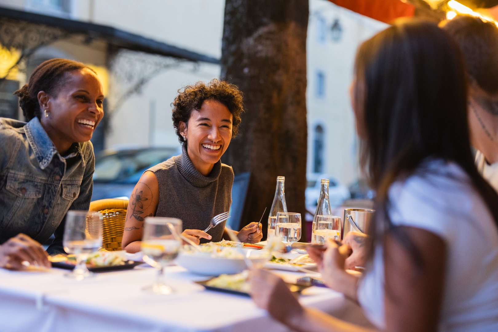 Group of cheerful young multi ethnic female friends enjoying dinner together, laughing and talking at an outdoor restaurant in lisbon, portugal, during summer evening