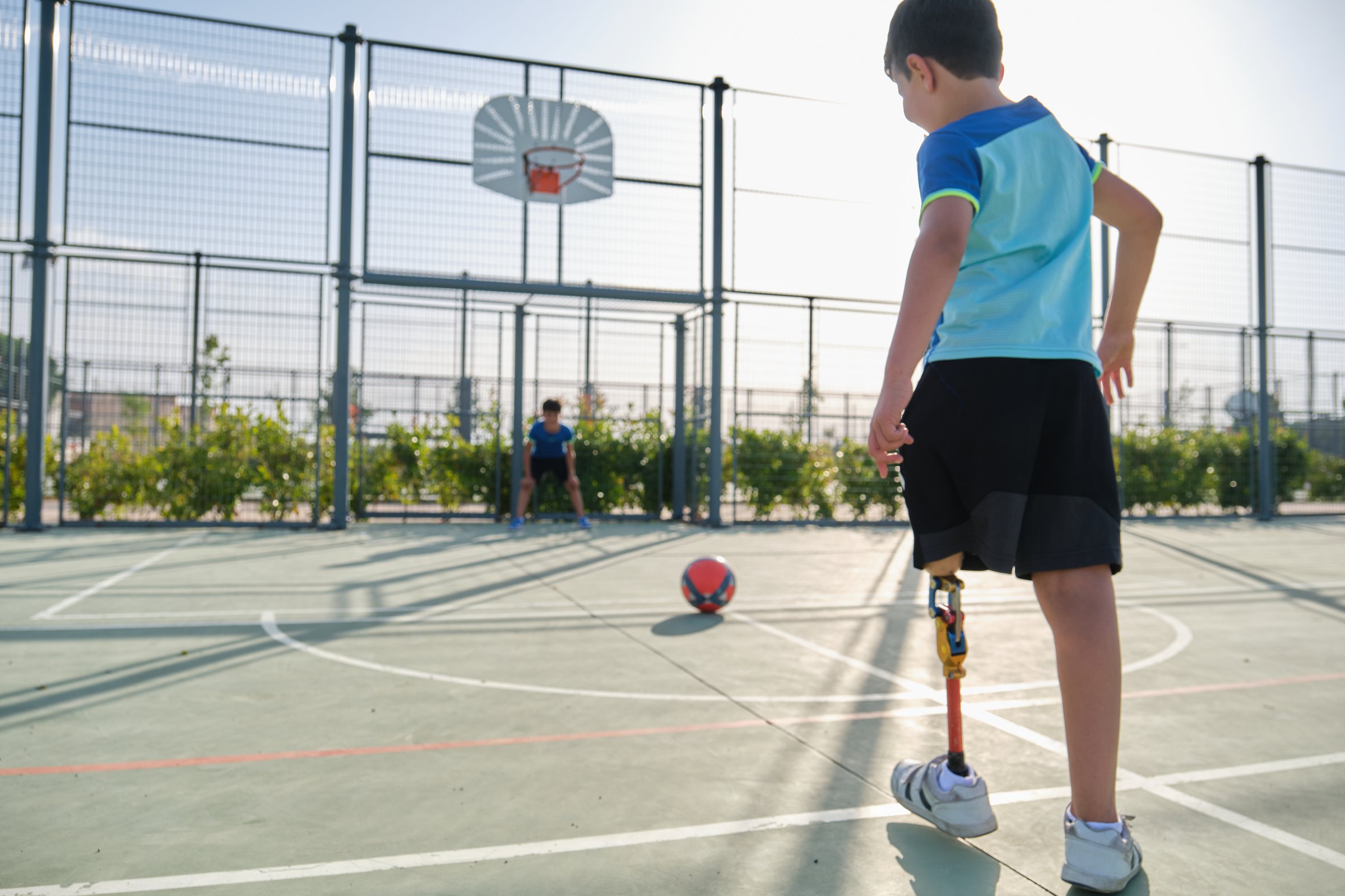 Two friends playing football, one of them has a leg prosthesis and is kicking a penalty. Kids playing sports together.