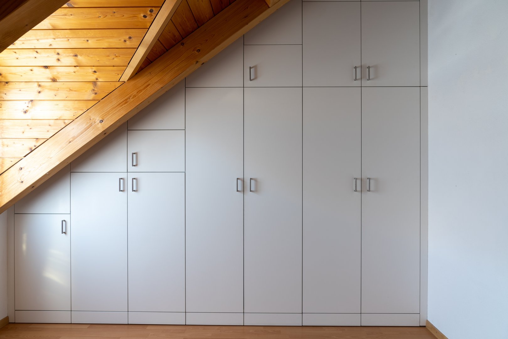 A interior view of a custom-made closet built into a master bedroom with a sloping roof