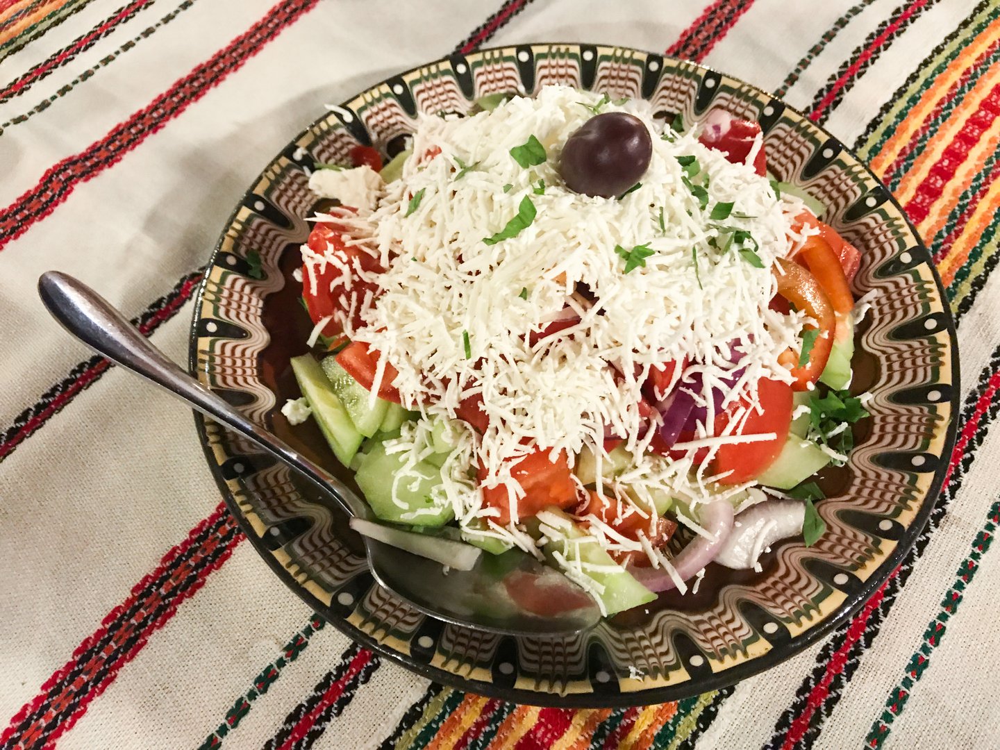 A large bowl with Shopsky salad of vegetables and cheese - the national Bulgarian food. Bowl and tablecloth with national ornaments