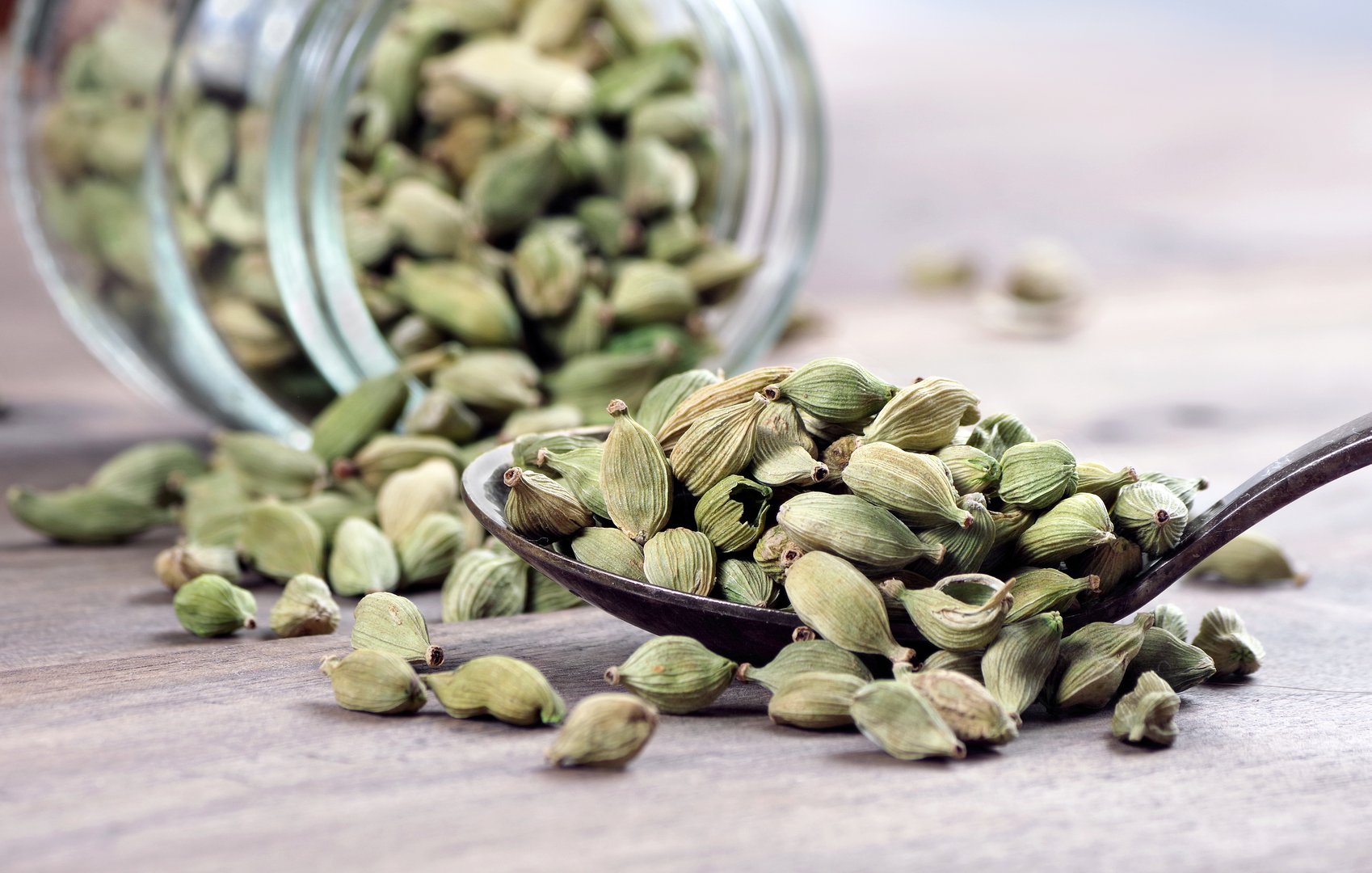 green cardamom pods in a spoon on a wooden table