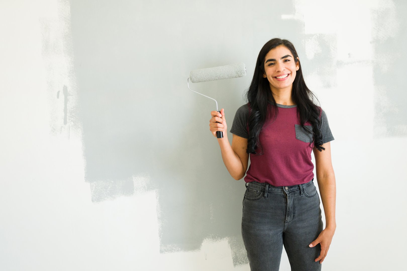 Beautiful woman is painting a gray accent wall in her new apartment and is happy with how it's turning out