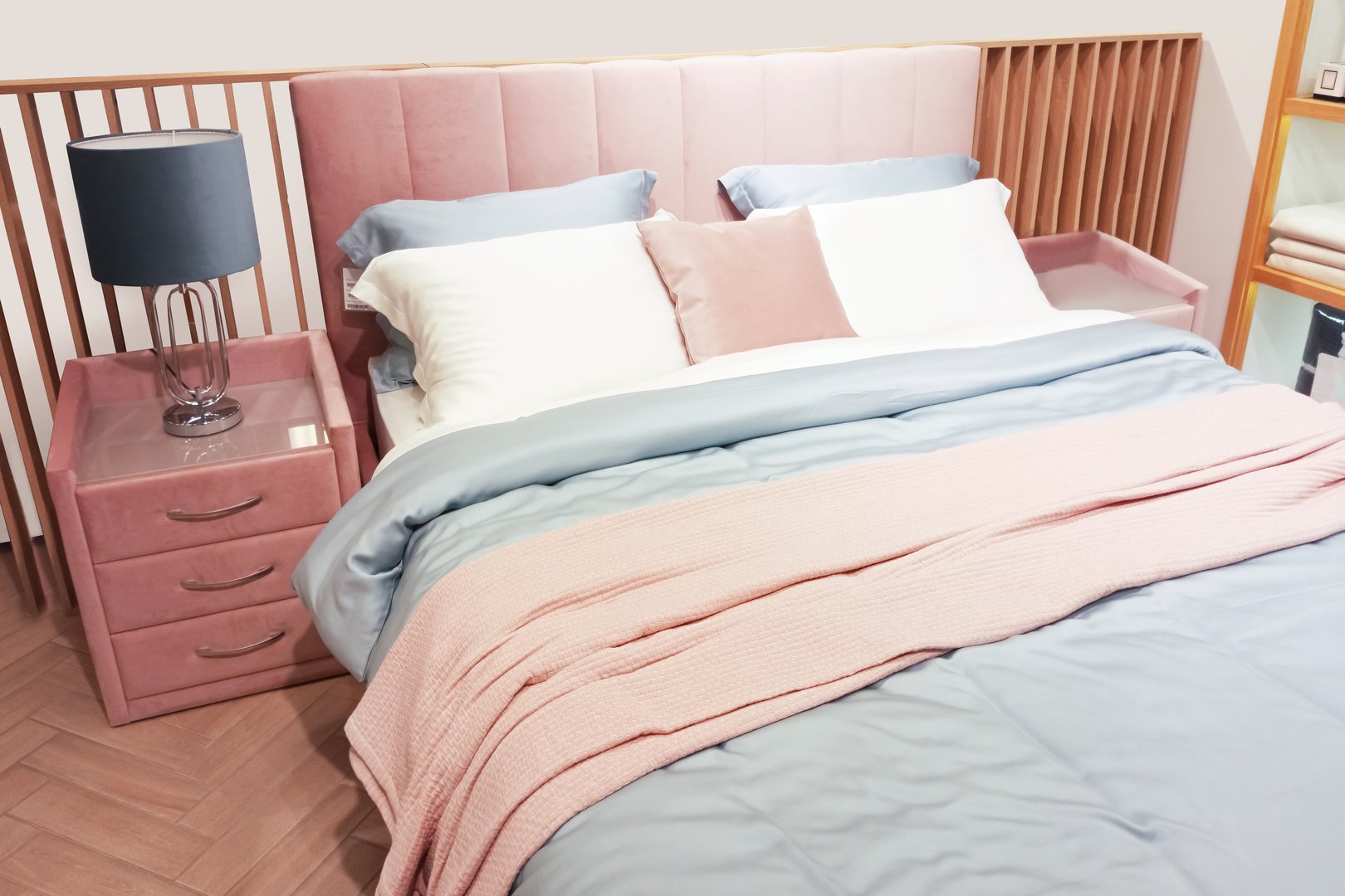 Bedroom interior. Bed with gray bedspread and pillows. Bedside tables upholstered in pink fabric.