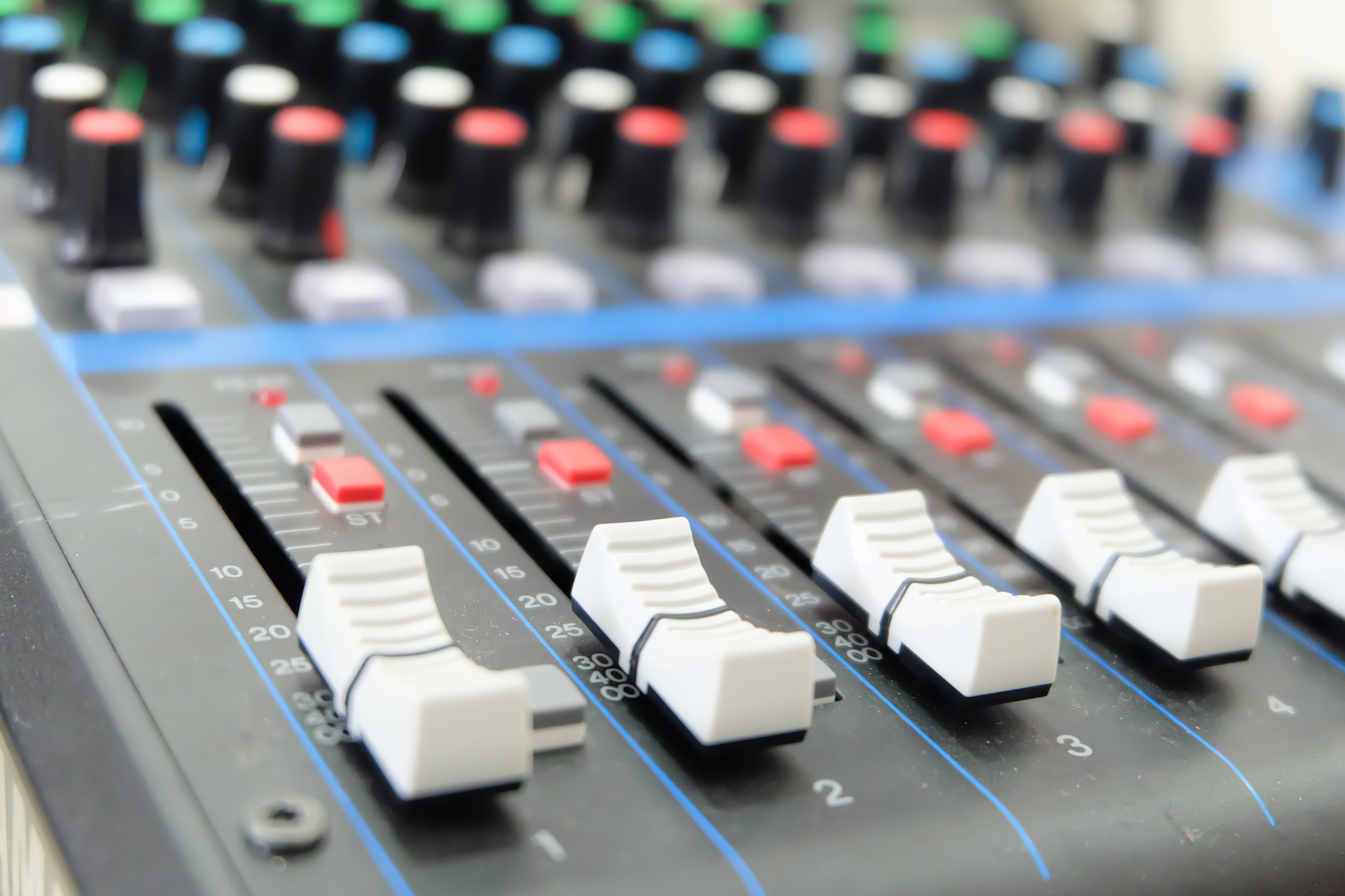 Professional sound mixing console shows channel faders in the foreground with a shallow depth of field Music production equipment