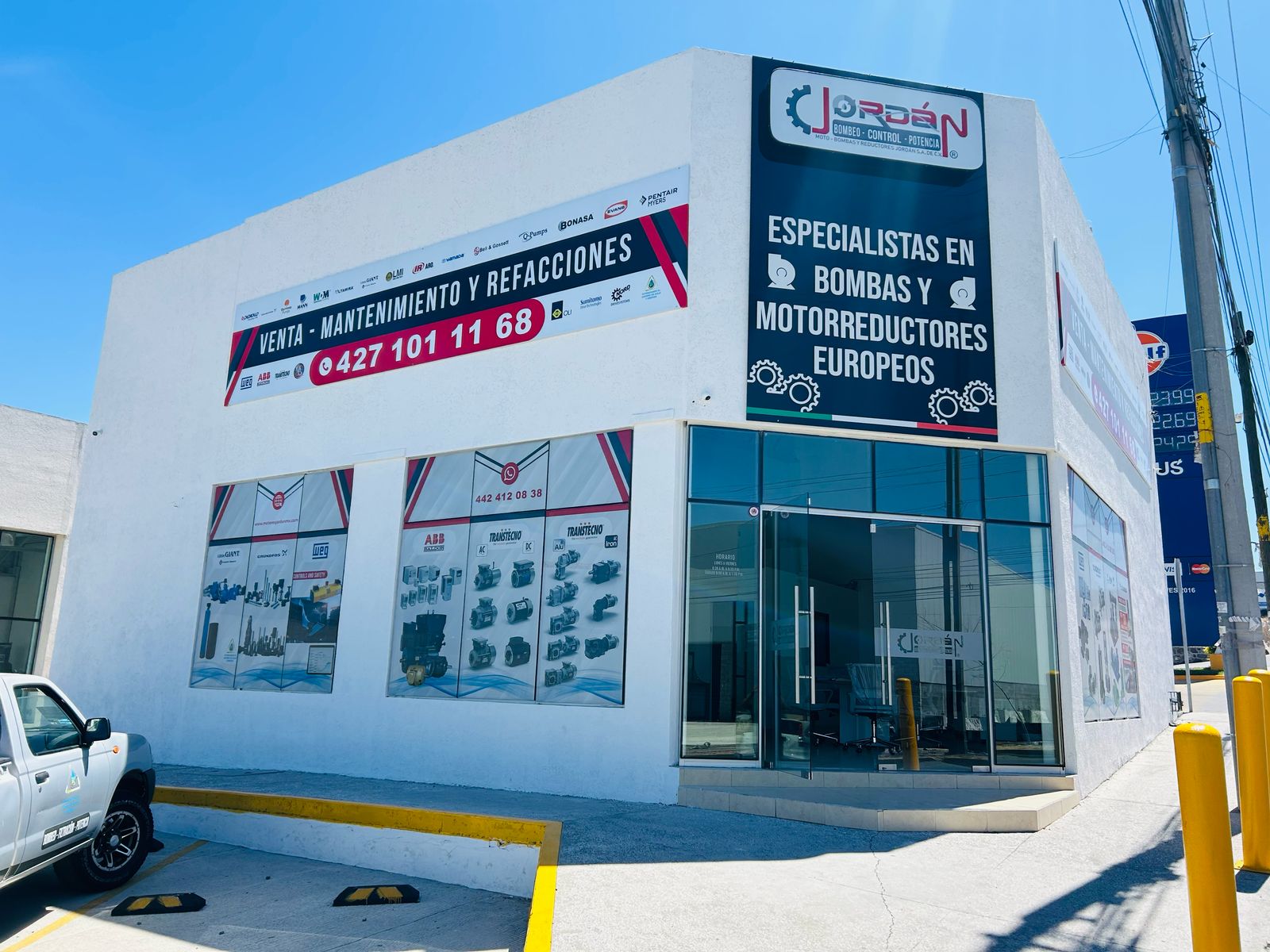 Commercial building with signs for a business specializing in pumps and motor reducers, featuring large windows and parking area.