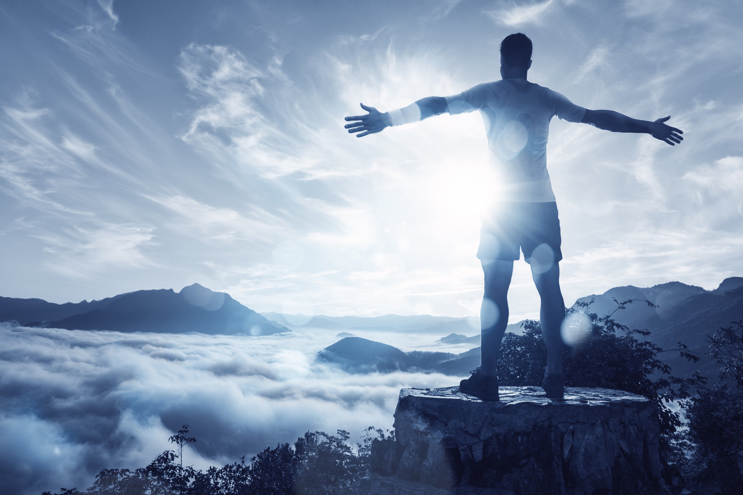 Man with spread arms standing in front of a mountain panorama - representing peak morning performance and cognitive optimization