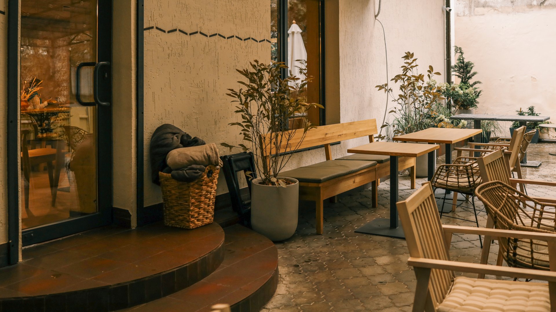 An inviting outdoor cafe scene featuring wooden tables and chairs, a bench, and decorative plants, creating a warm and welcoming ambiance.