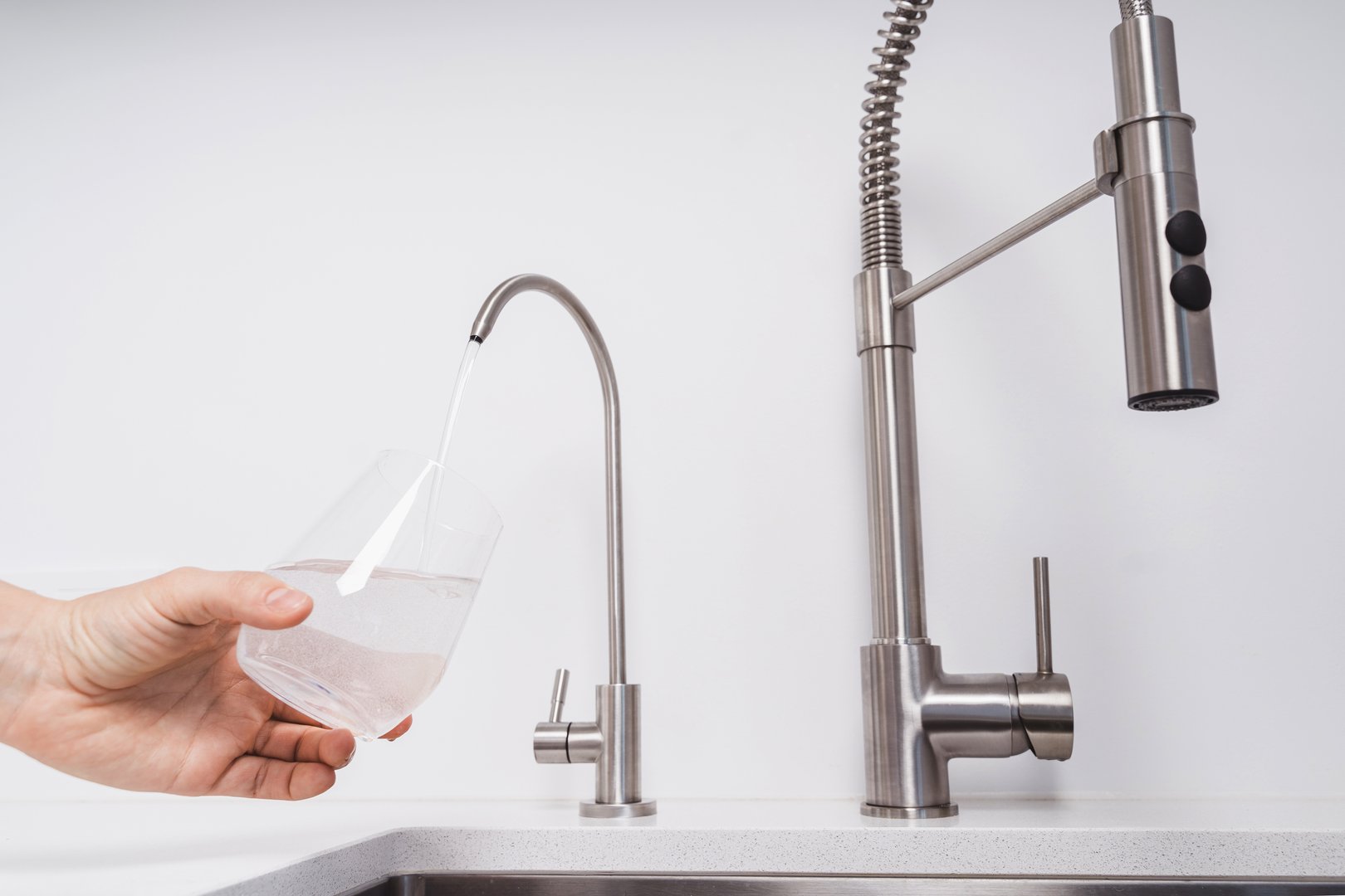 Woman dispensing filtered water from stainless steel tap into glass