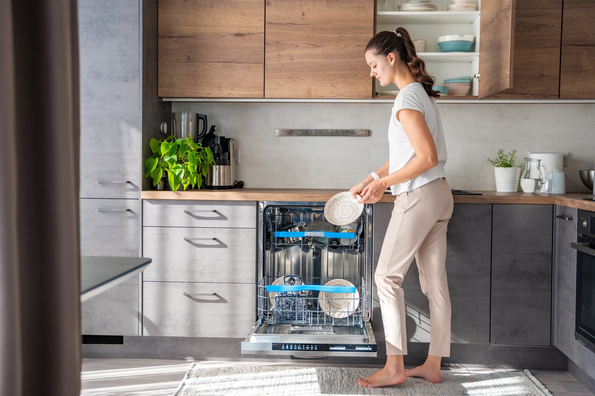 A woman removes clean ceramic dishes from the dishwasher. Household and useful technology concept. High quality photo.