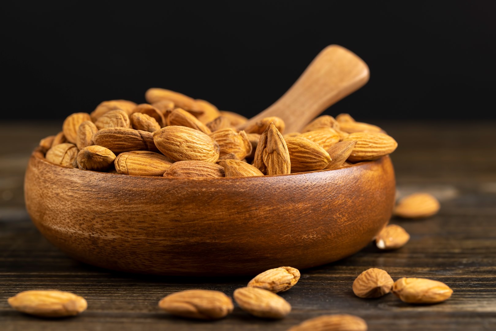 yellow whole nuts of unroasted almonds with a wooden spoon on the table, a large number of hard raw almonds on the table during cooking