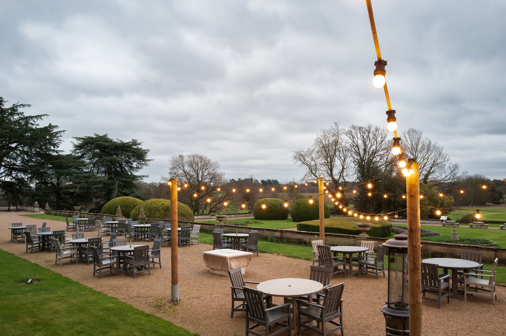 Warm string lights seen strewn above a large outside dining area at a country house in rural setting