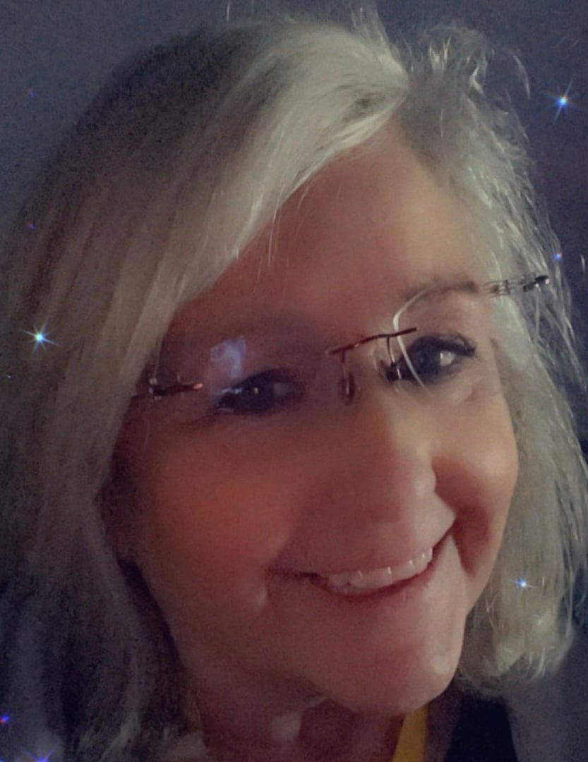 A smiling woman with gray hair wearing glasses, captured in a close-up selfie with a filter showing sparkles.