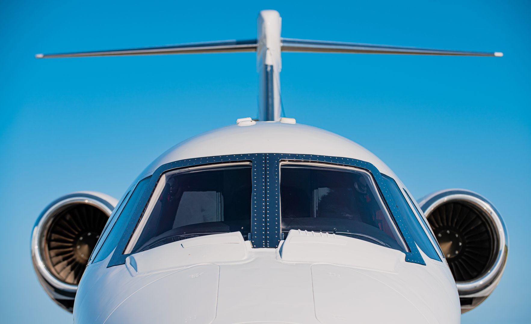 Nose and cockpit and two high mounted engines of a small business jet. Focus is on the cockpit front windows with the high mounted jet engine in soft focus at the back.