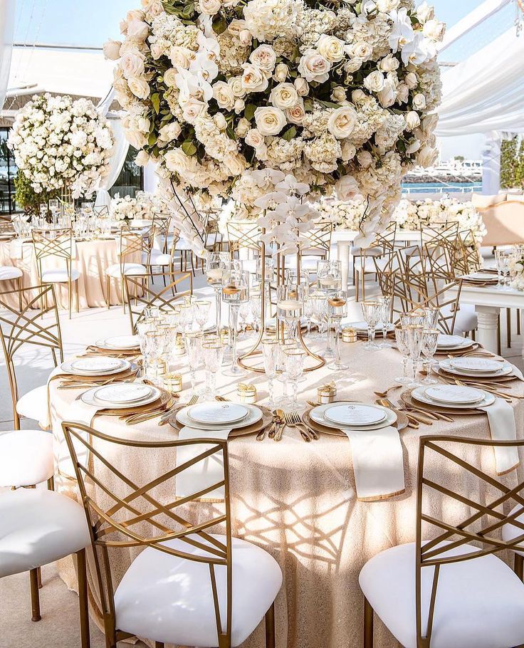 Elegant wedding reception setup with a round table, floral centerpiece, gold accents, and ornate chairs.