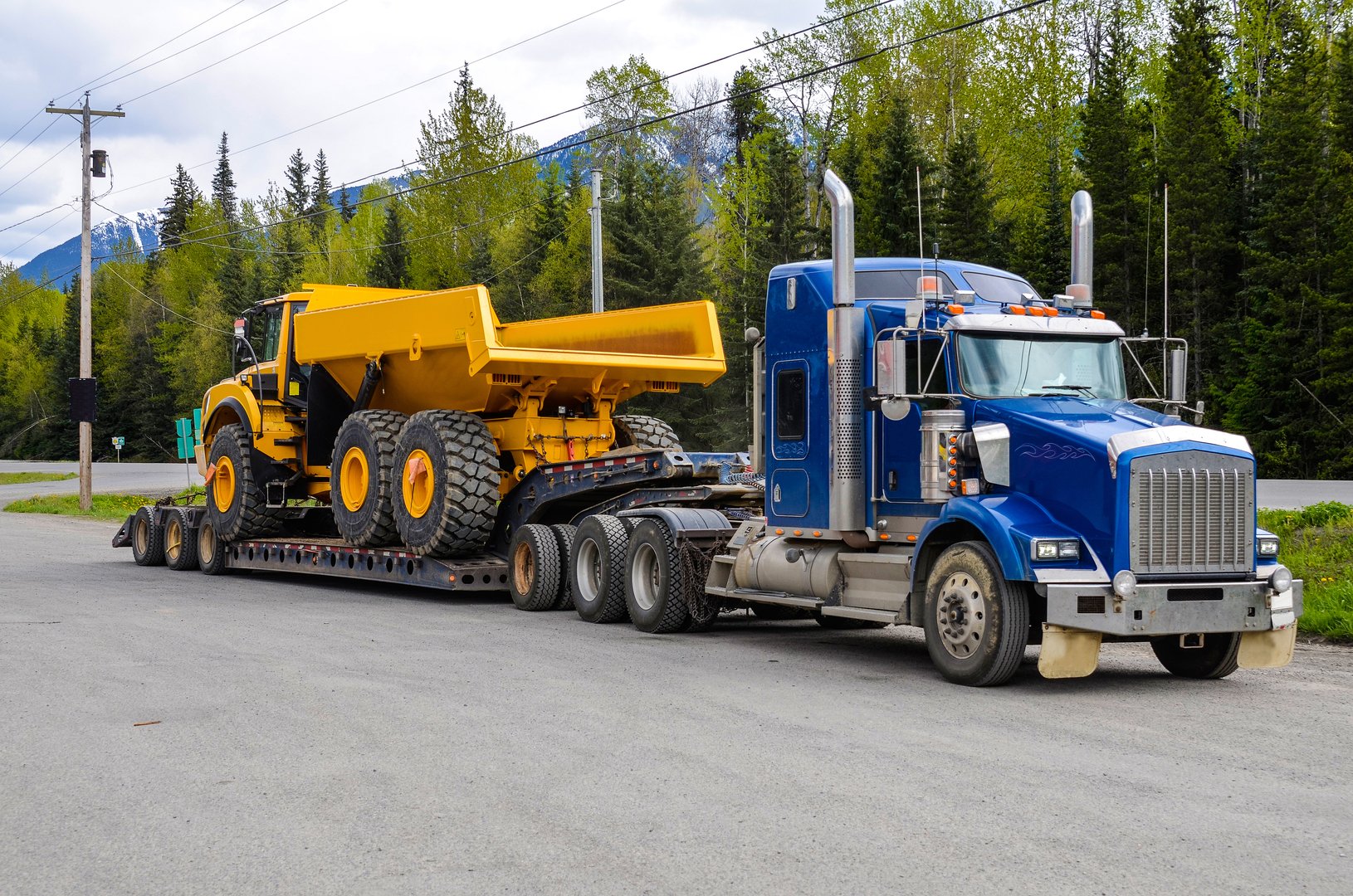 Big truck with a low platform trailer carrying a tipper truck on a public parking area of a truck stop